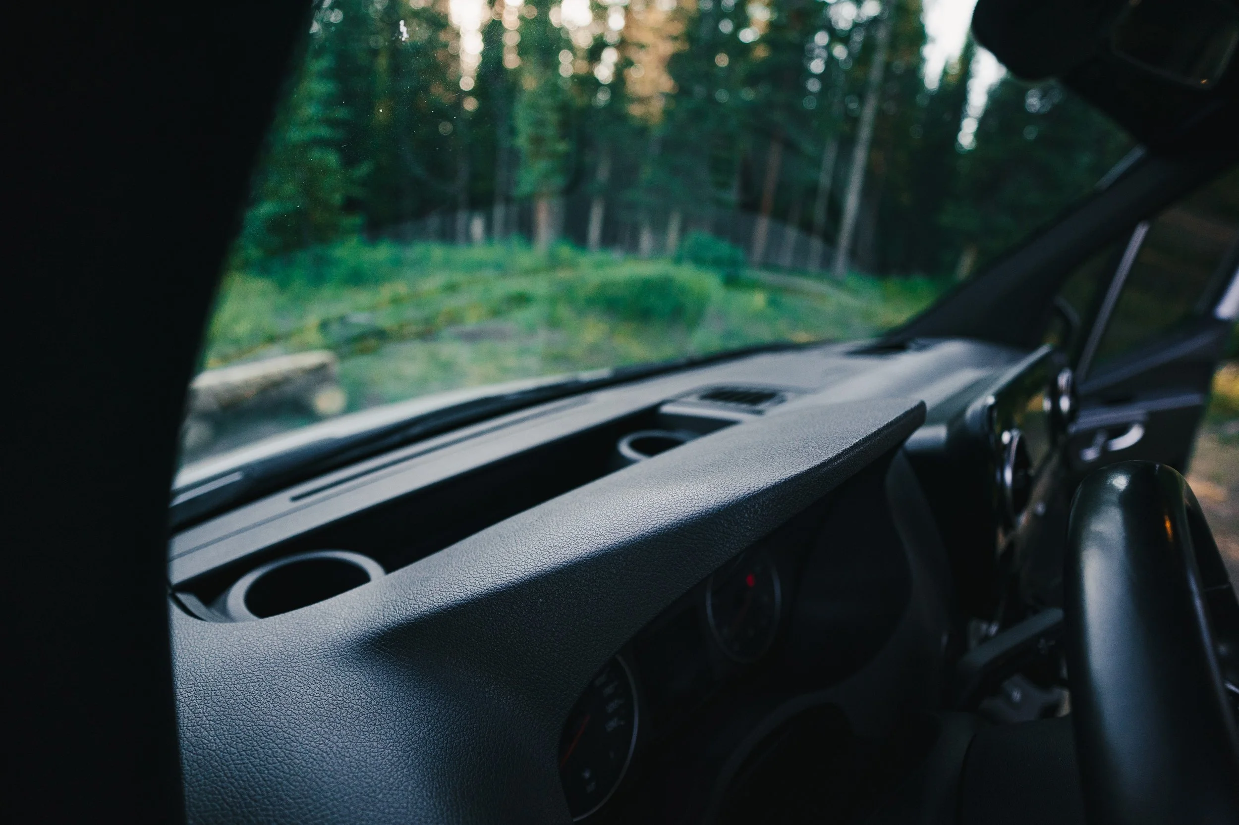 Close-up of a vehicle's dashboard with a view of a forest through the windshield.
