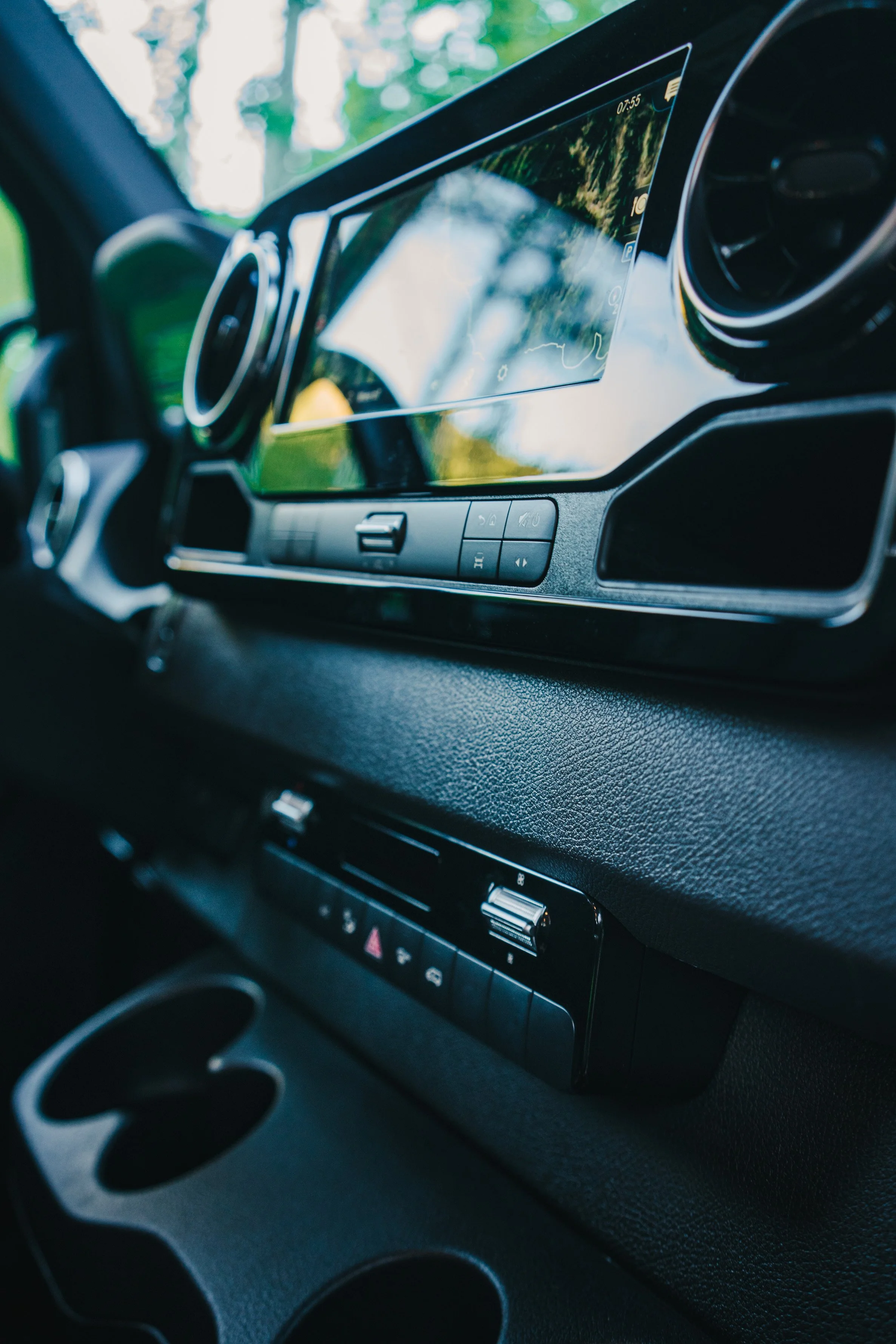 Close-up of a vehicle dashboard with a digital infotainment screen displaying a map, air vents, and control buttons.