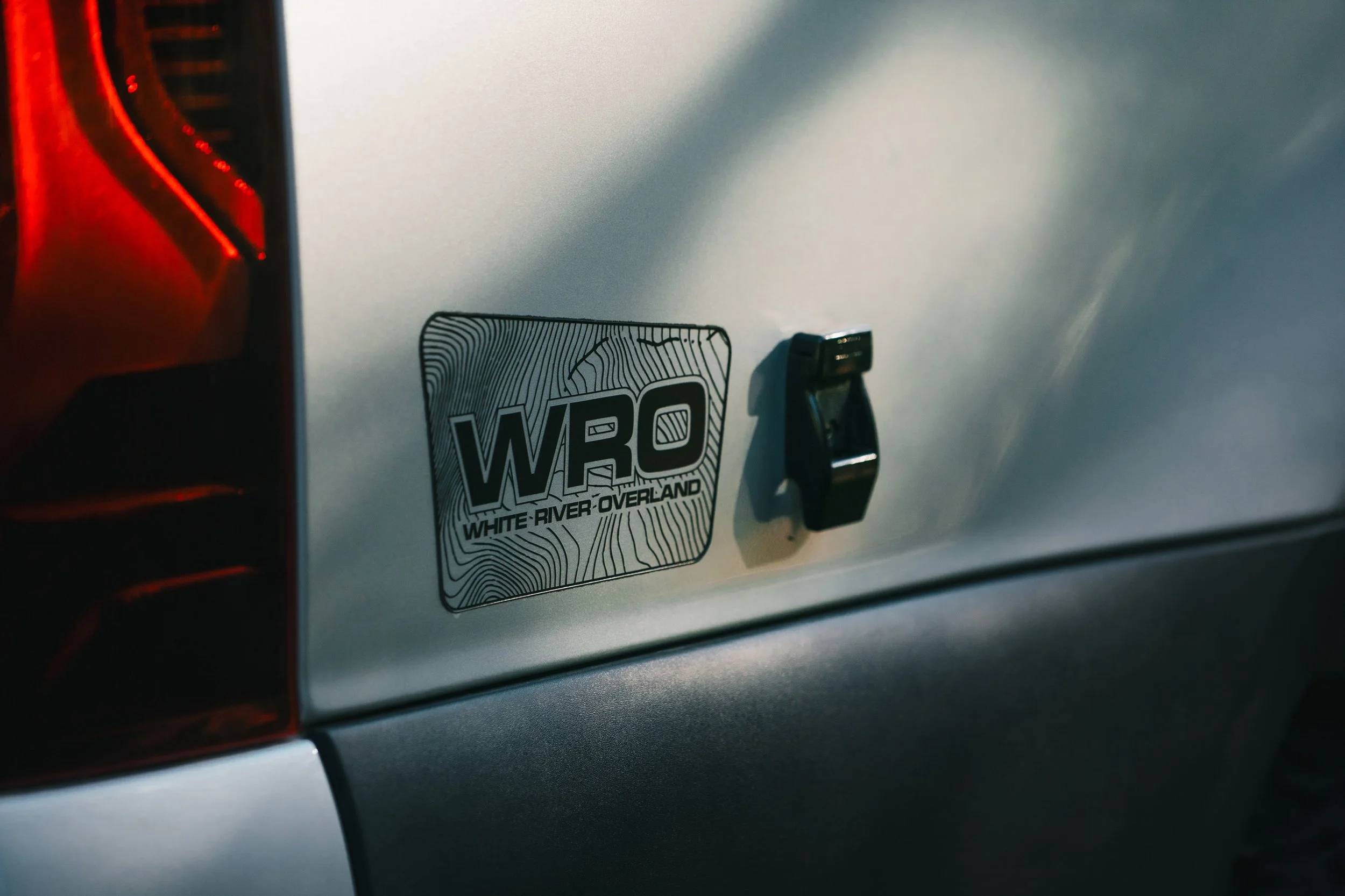 Close-up of a silver vehicle's rear with a WRO (White River Overland) sticker and a black latch handle.