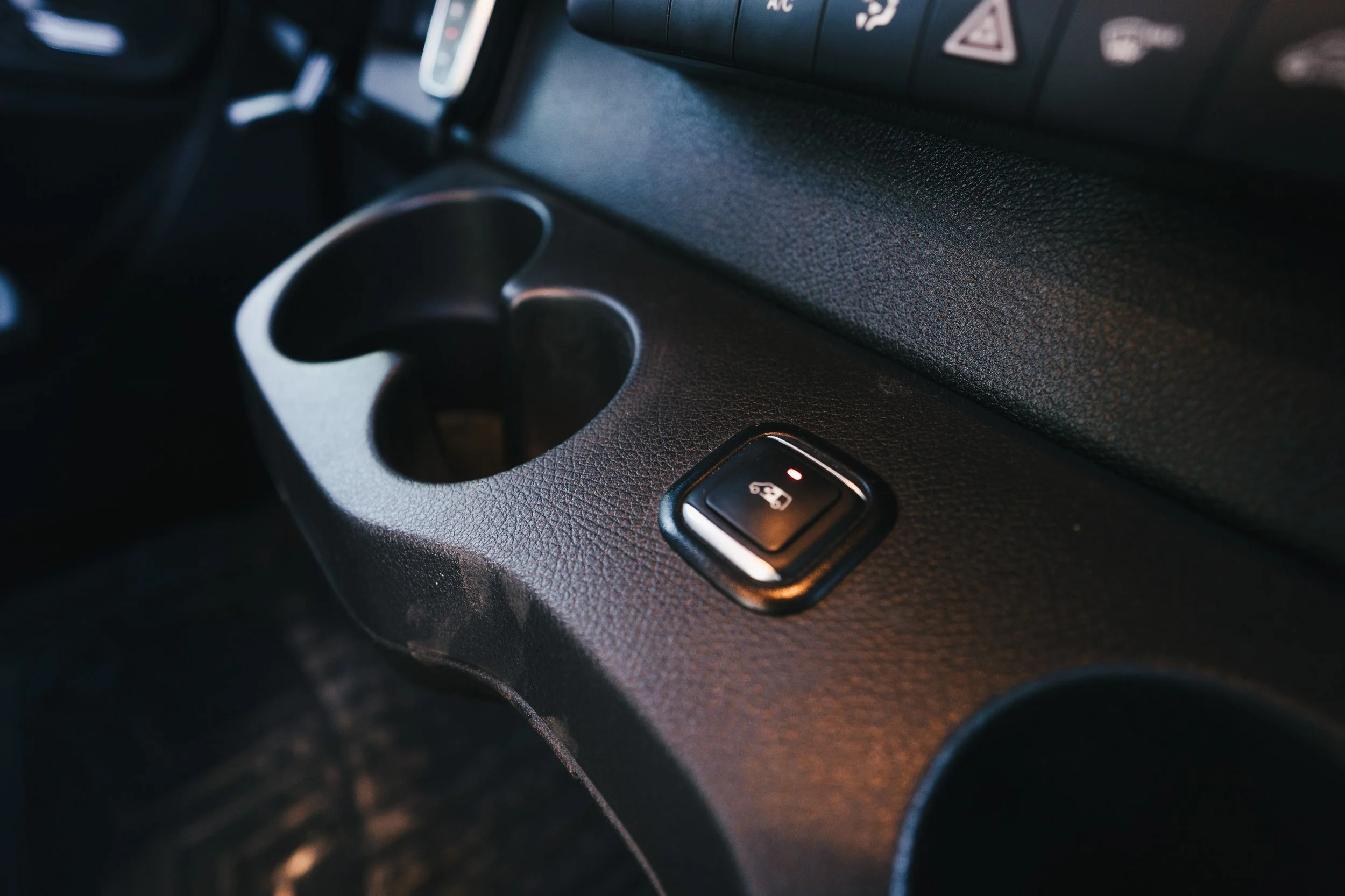 Close-up of a car interior with a cup holder and a child safety lock switch on the dashboard.