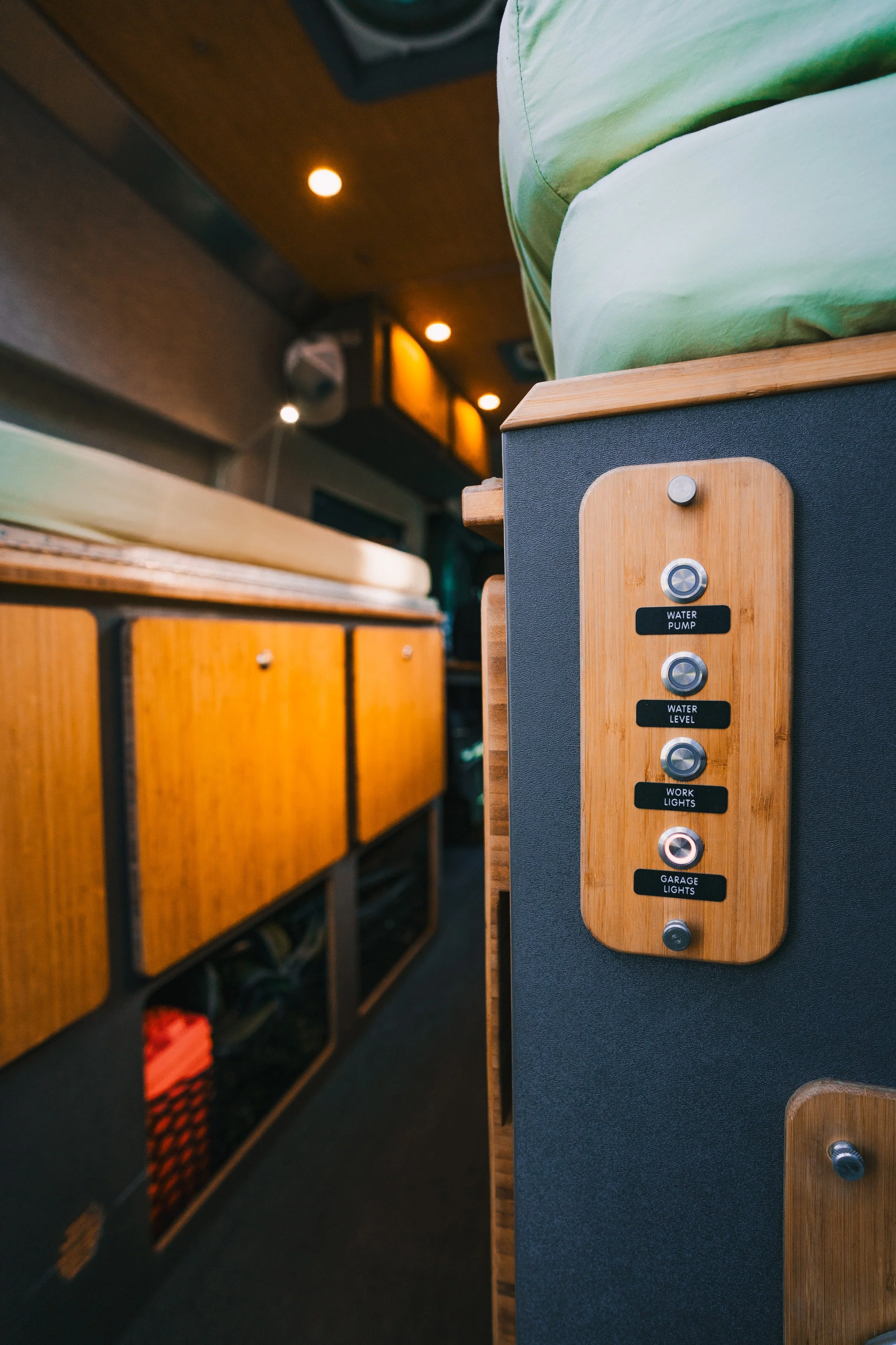 Close-up of a wooden control panel with labeled buttons for water pump, water level, work lights, and garage lights inside a vehicle.