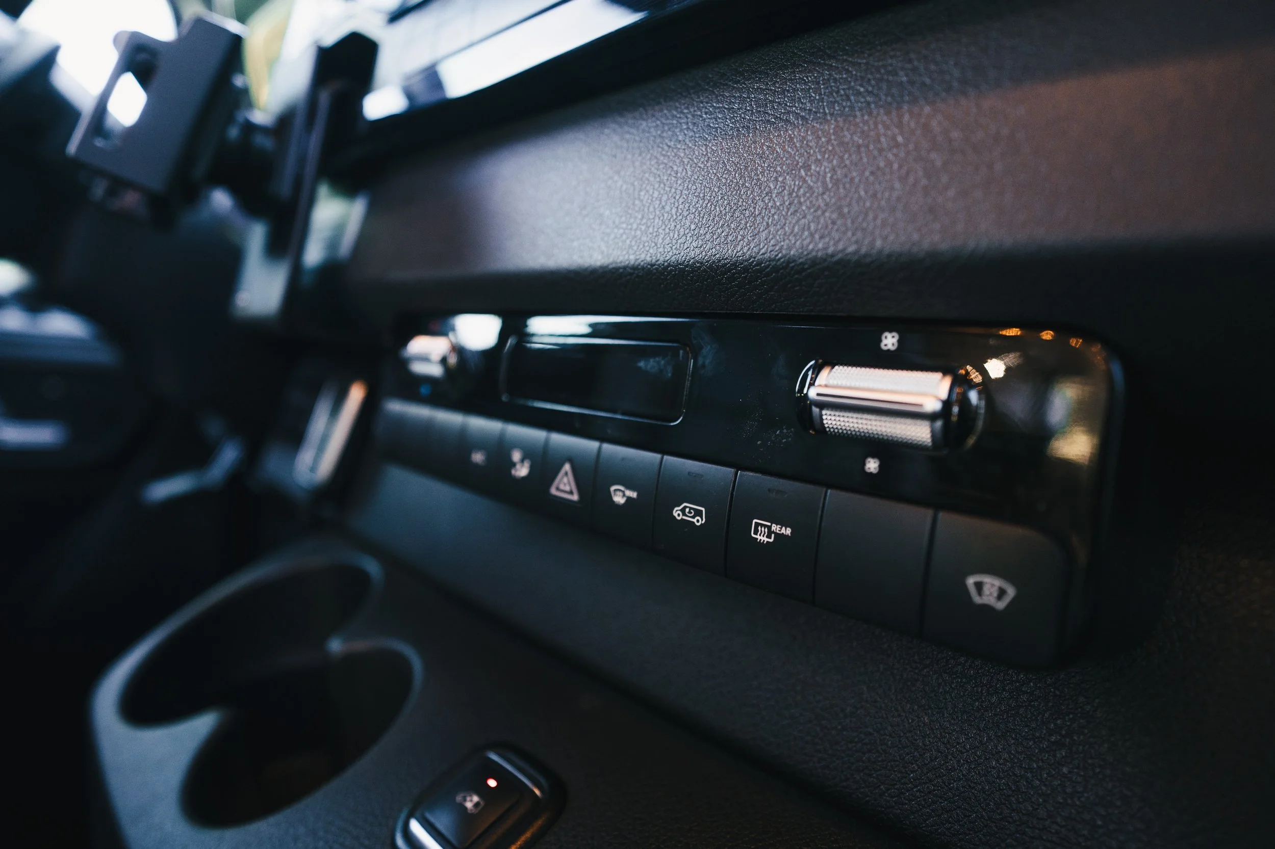 Close-up of a vehicle dashboard with various control buttons and a switch, including hazard lights, rear window defrost, and windshield wiper controls.