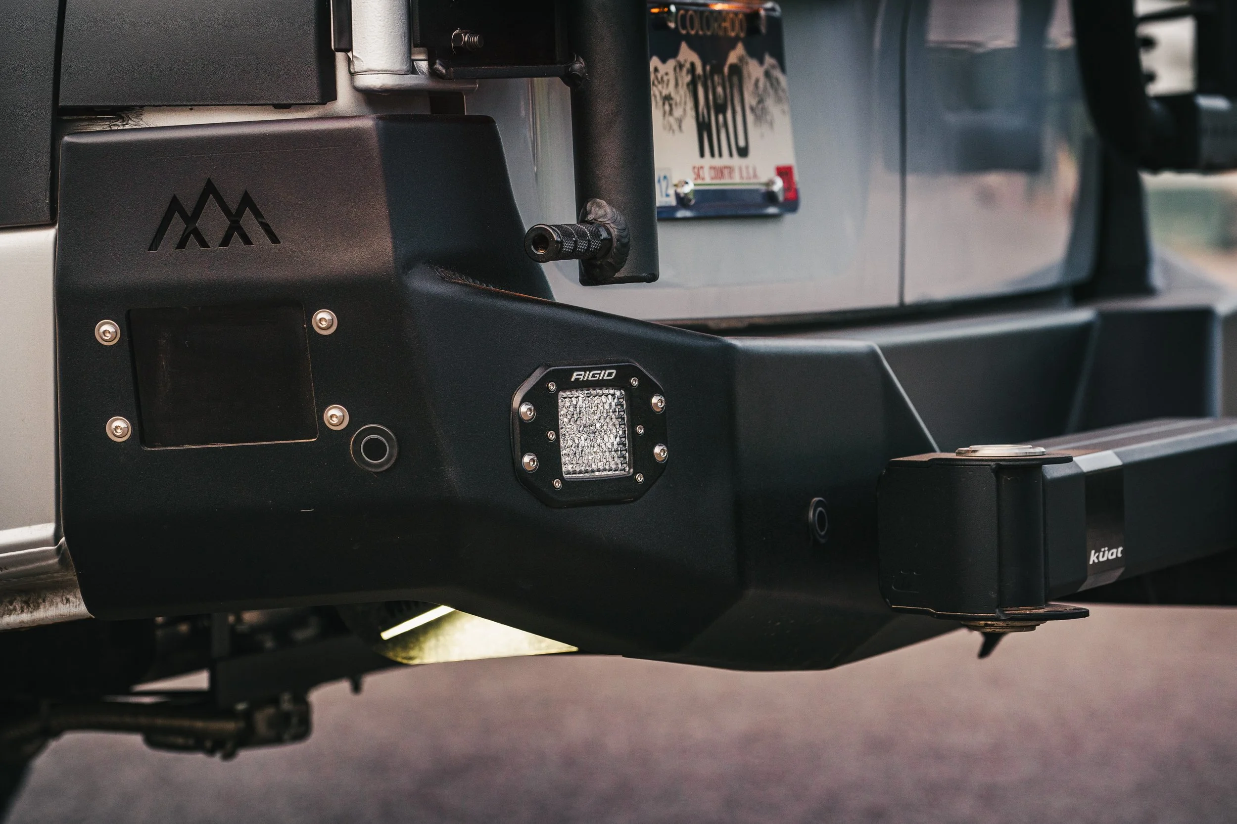 Close-up of a vehicle's front bumper with a mounted LED light, a black winch, and a Colorado license plate.