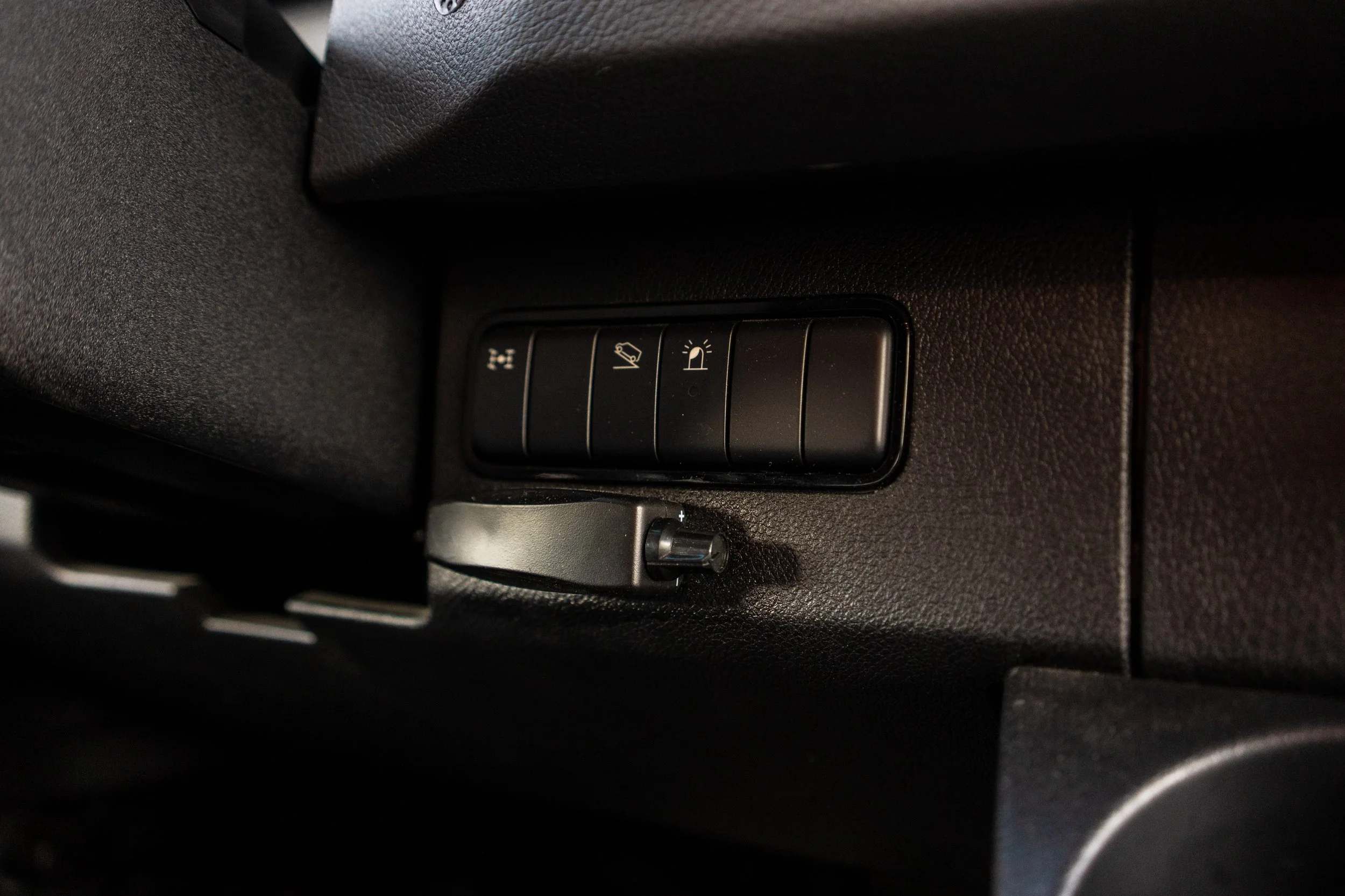 Close-up of four buttons on a car dashboard, with icons for various vehicle functions, and a small rotary dial below them.