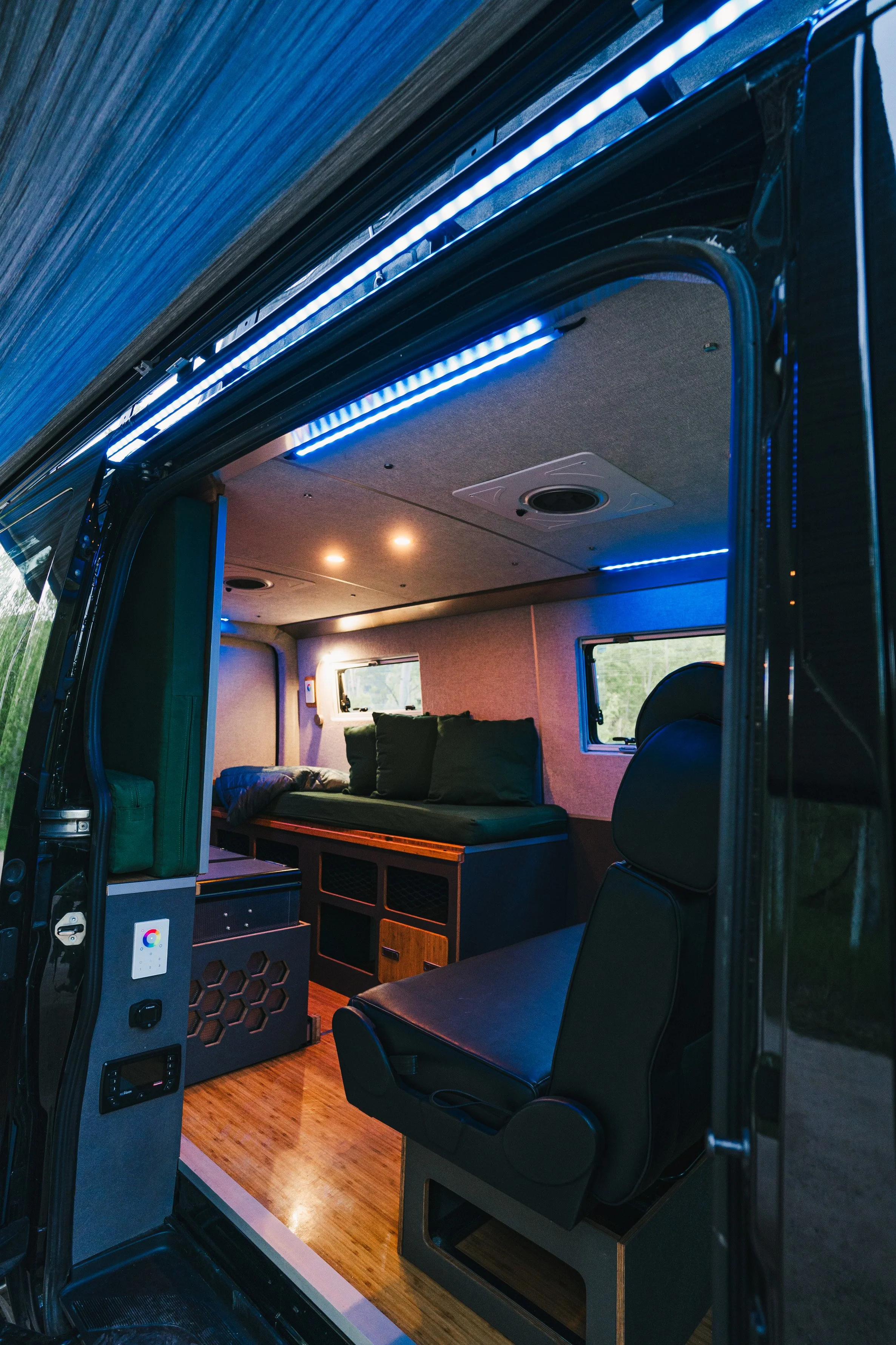 Interior of a camper van with a bed, window, and LED lighting.