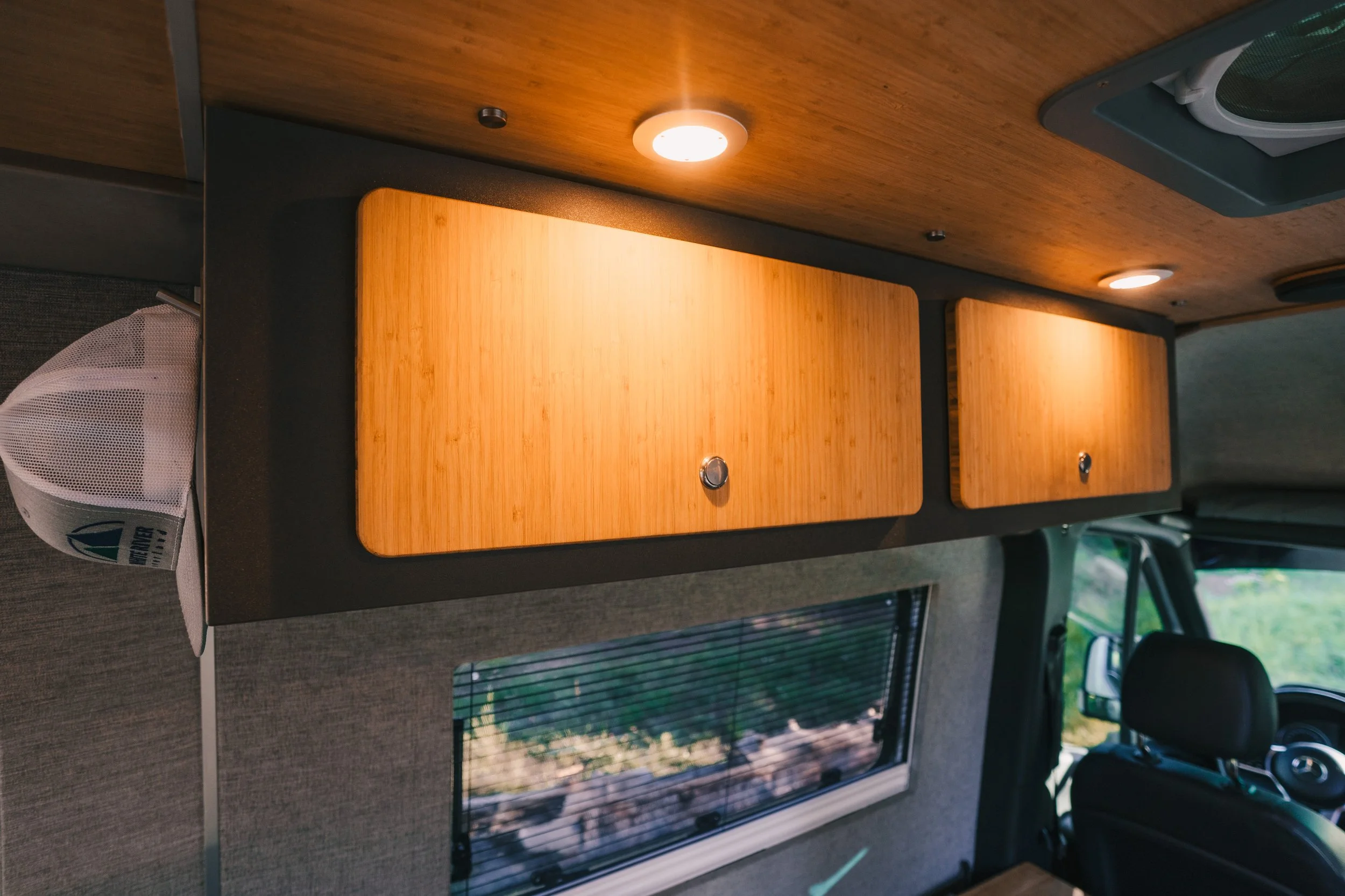 Wooden cabinet doors inside a vehicle, with ceiling lights and a small window below.