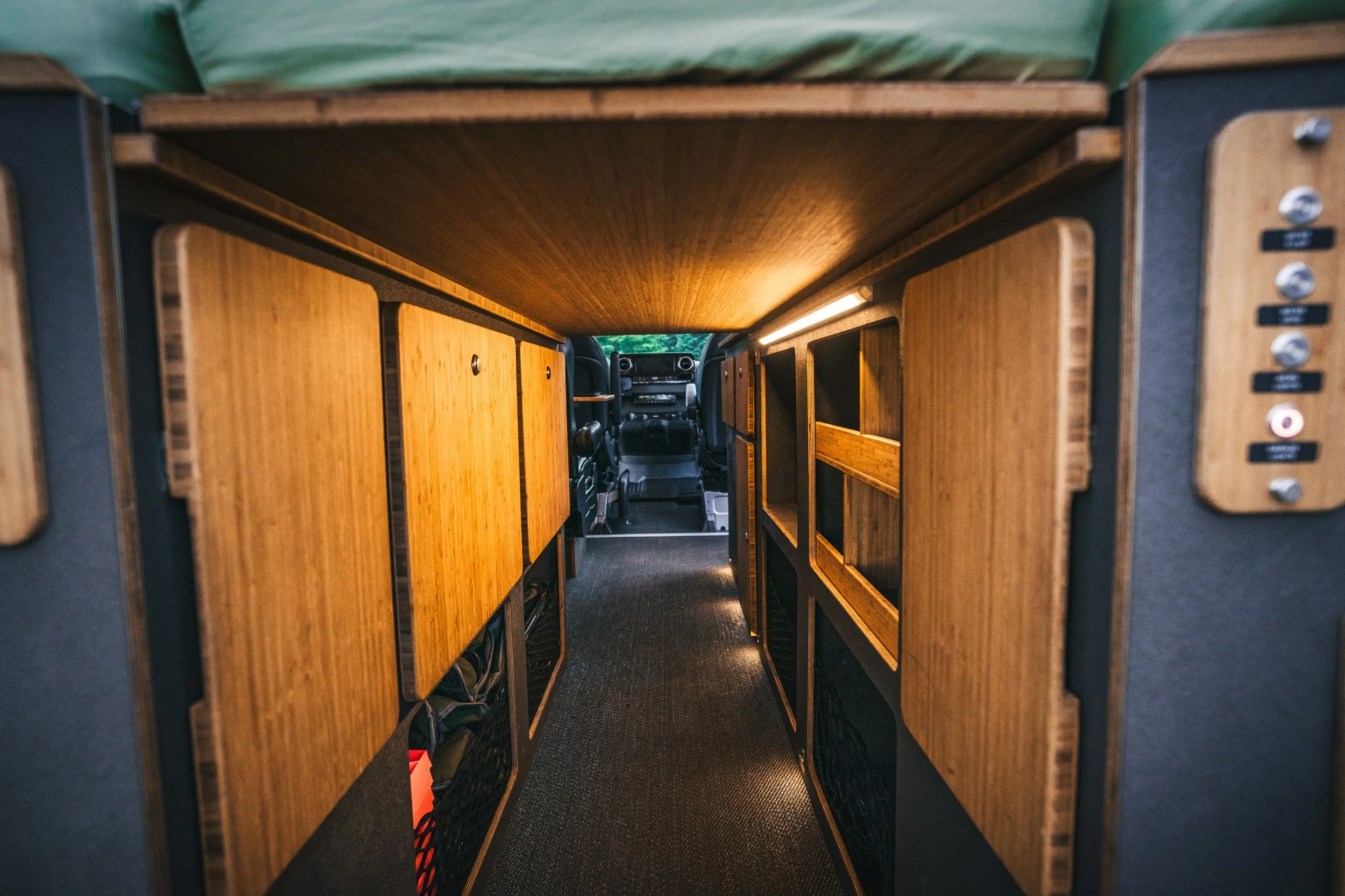 Inside view of a camper van with wood-paneled cabinets and narrow corridor leading to the driver's cockpit.