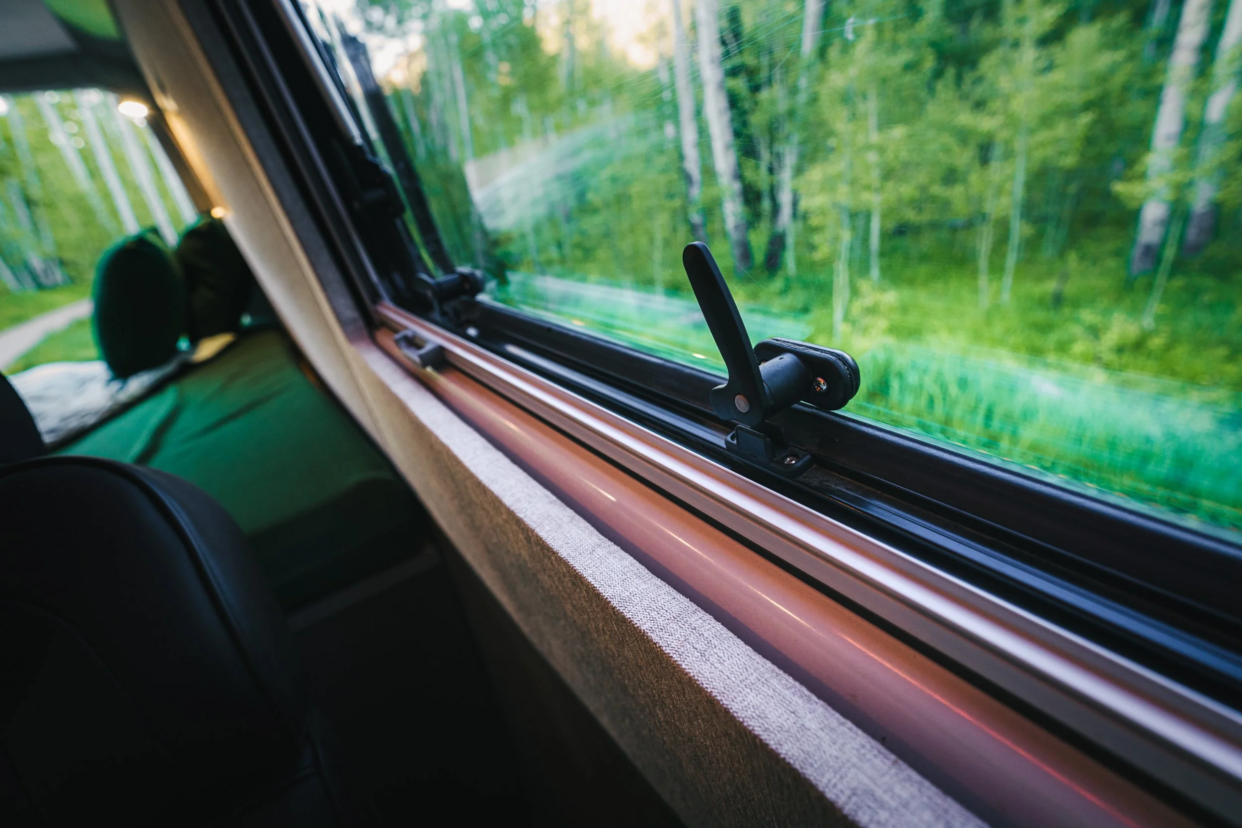 Inside view of a bus with an open window showing a green forest landscape outside.