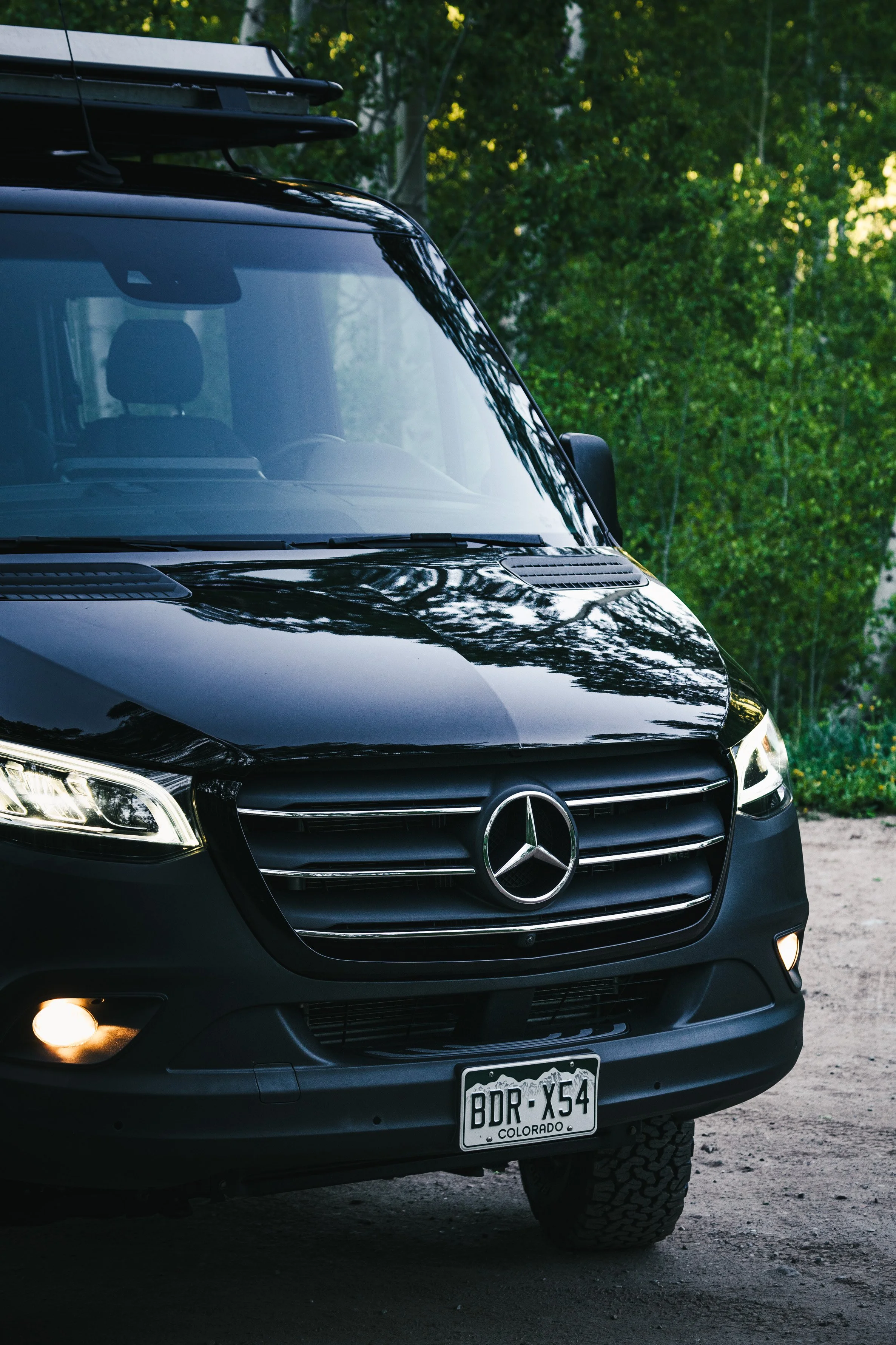 Black Mercedes-Benz van parked on a dirt road with trees in the background.