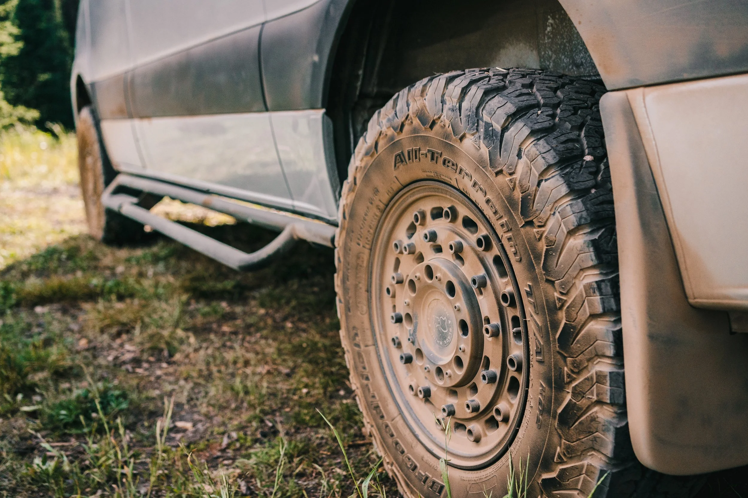 Close-up of a large off-road tire on a dusty vehicle parked on grass.