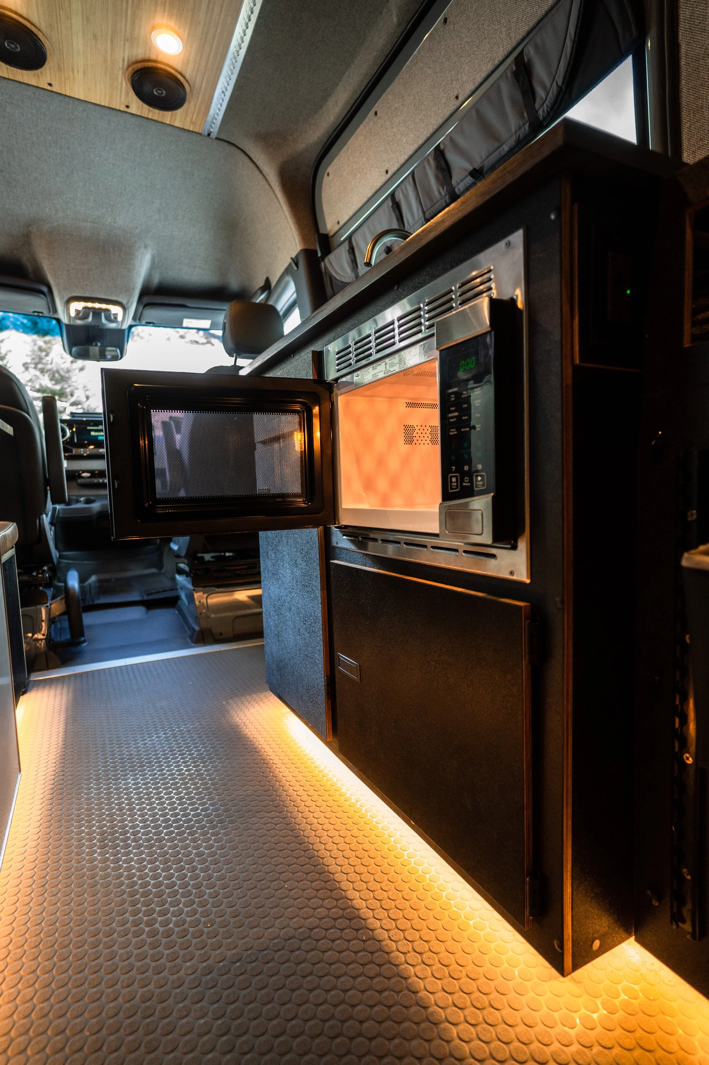 Interior of a camper van with a microwave oven, illuminating the floor with warm lighting.