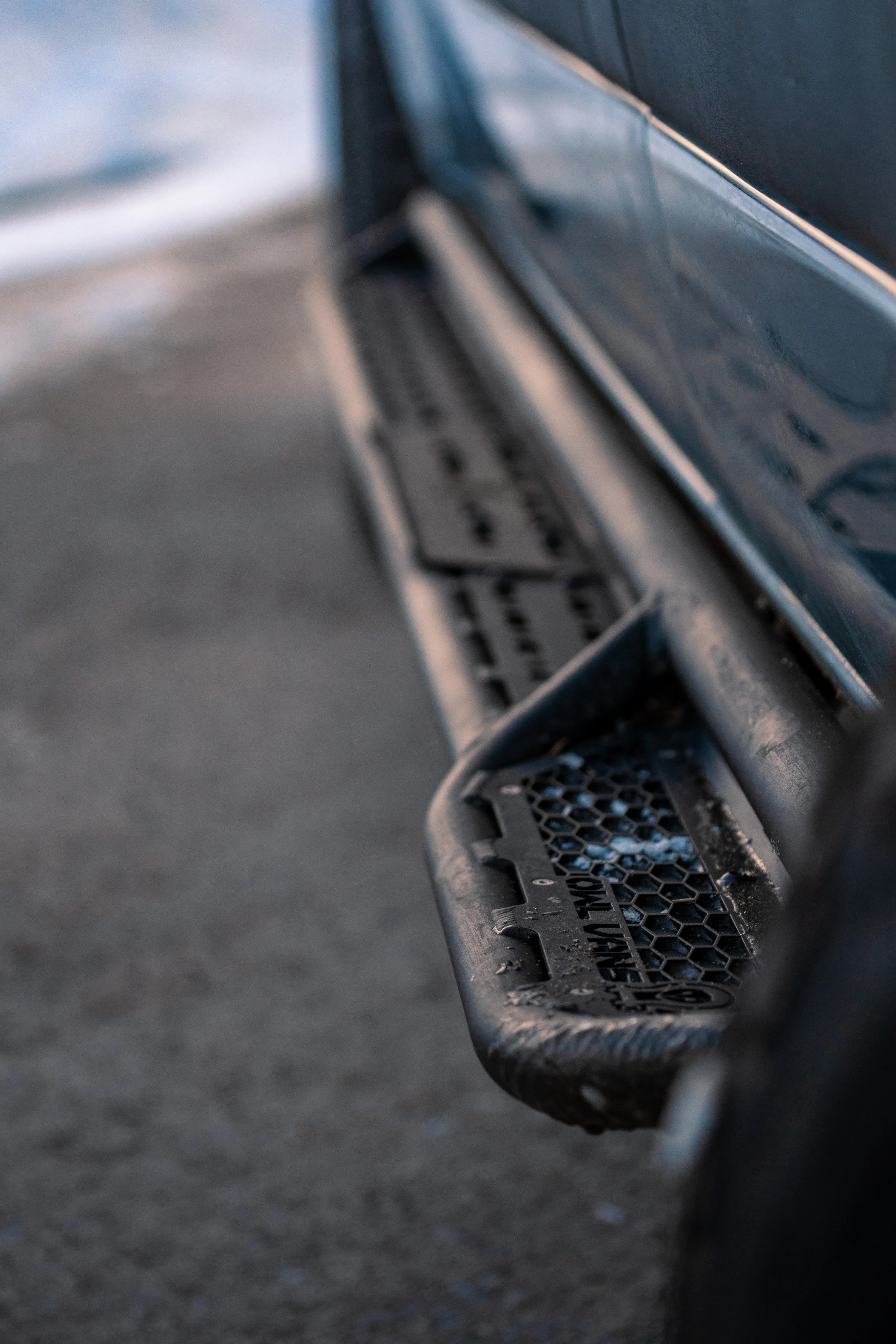 Close-up of the side step of a black vehicle, with tire marks on the ground nearby.
