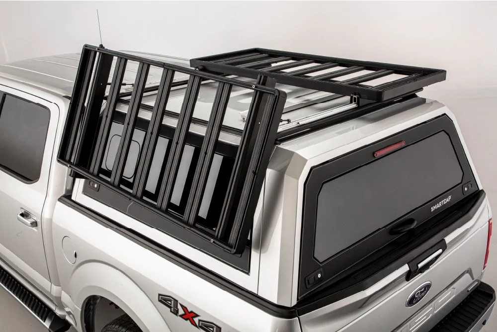 A white pickup truck with a black truck cap and a black metal roof rack on top.