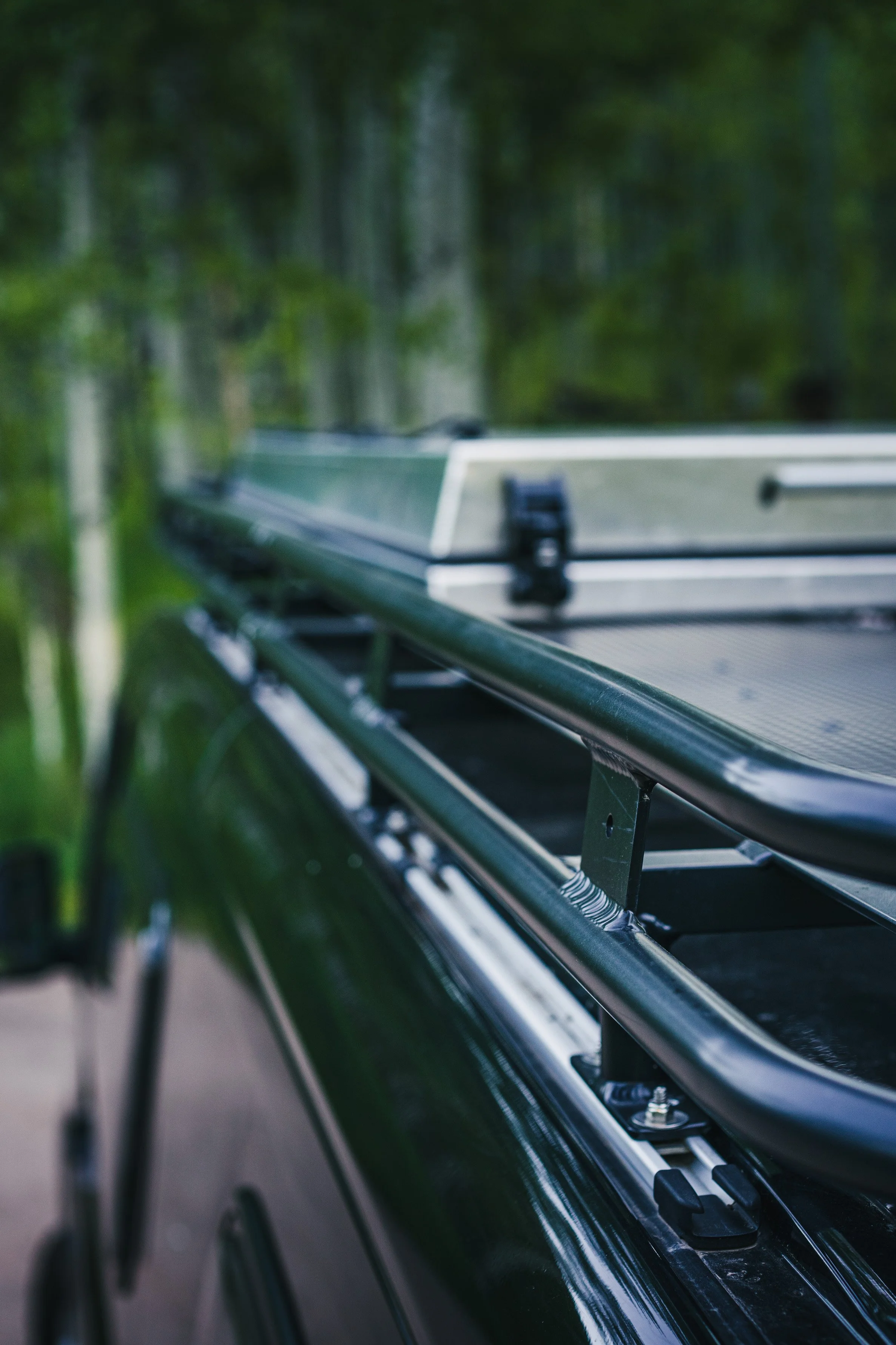 Close-up of a vehicle roof rack with a mounted boat in a green, wooded area.
