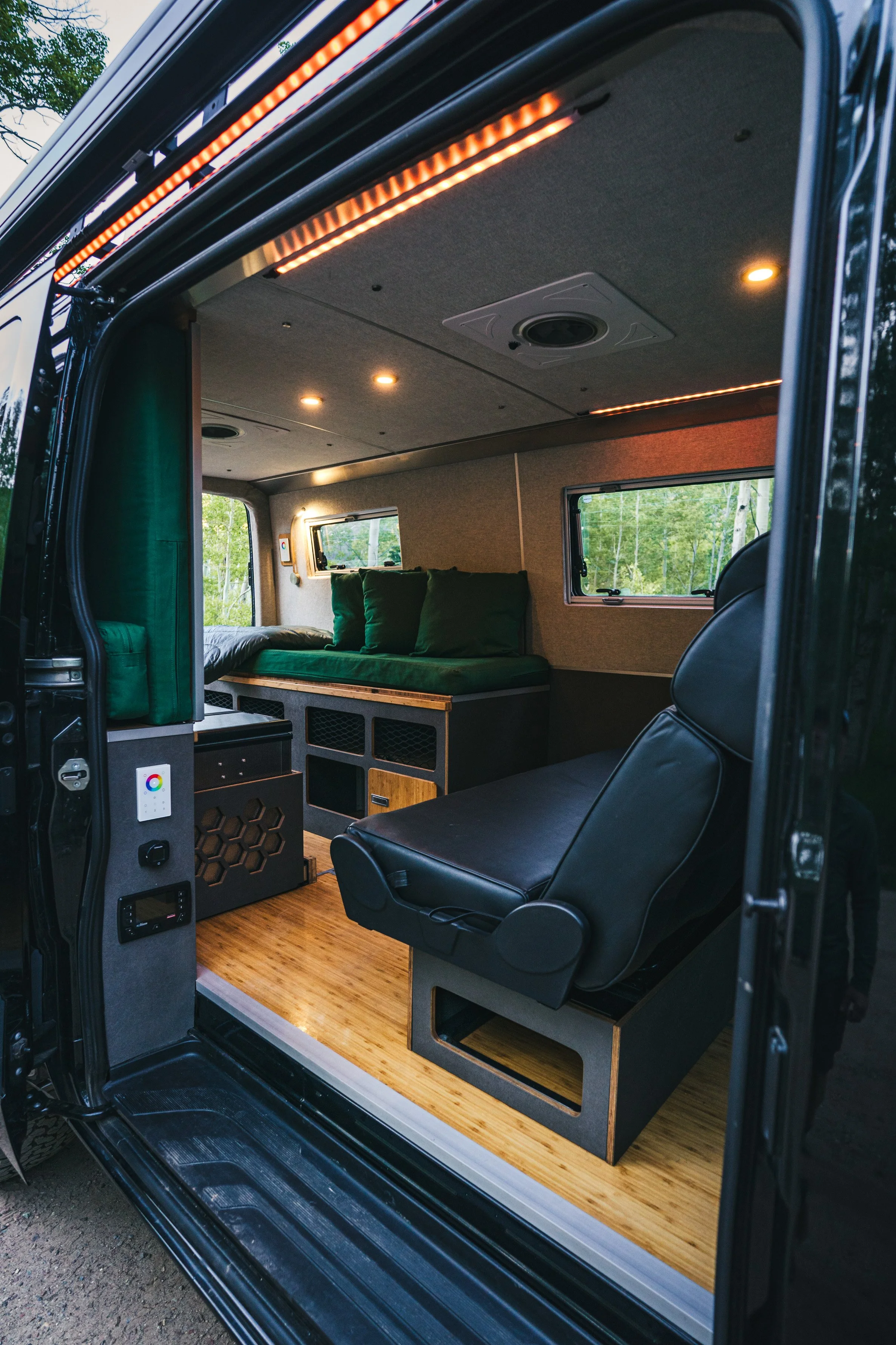 Interior of a custom van with green cushions, a black leather seat, windows, and wood flooring.