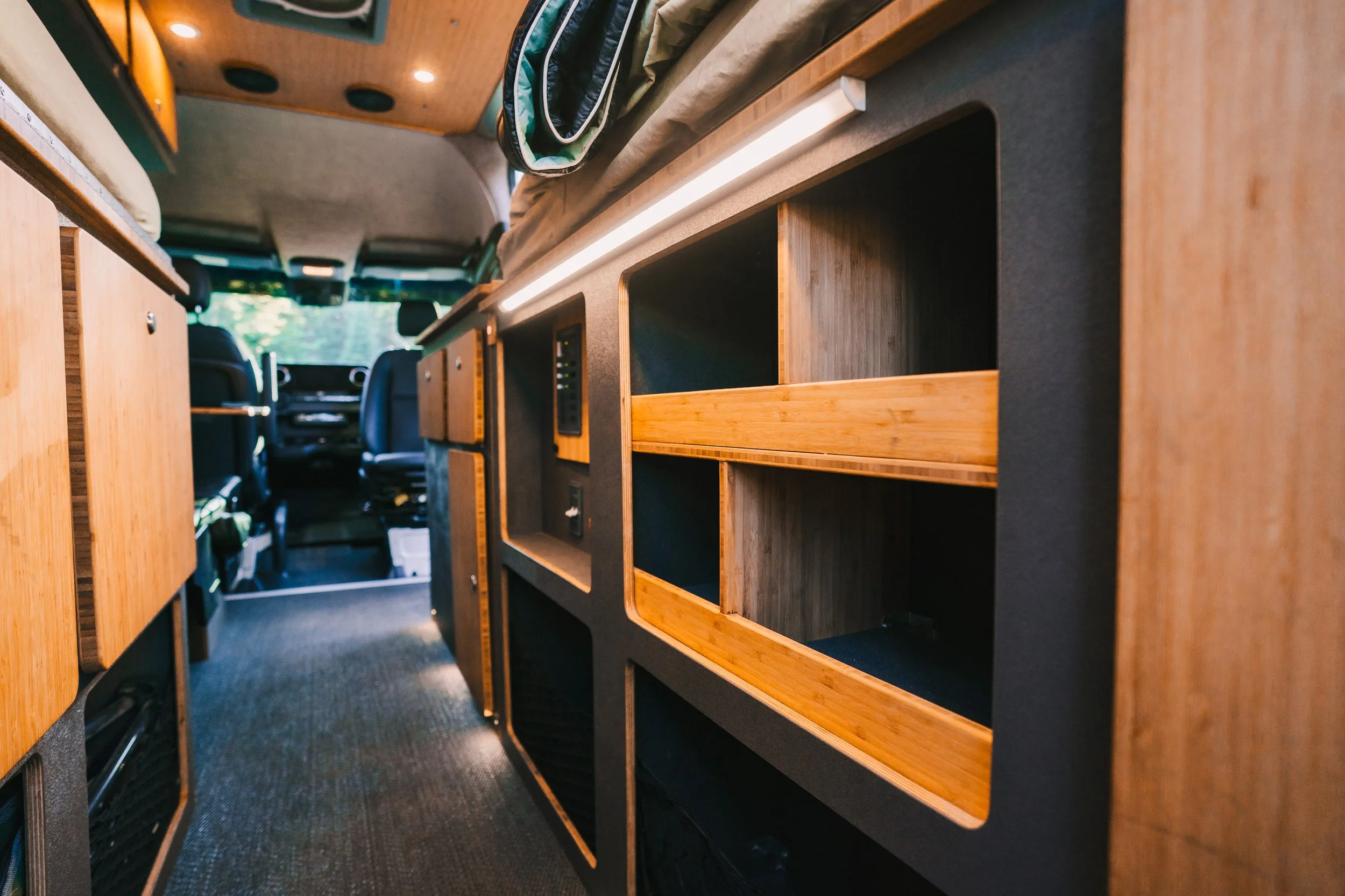 Inside a van or camper with wooden shelving and storage compartments, with the driver's seat and steering wheel visible in the background.