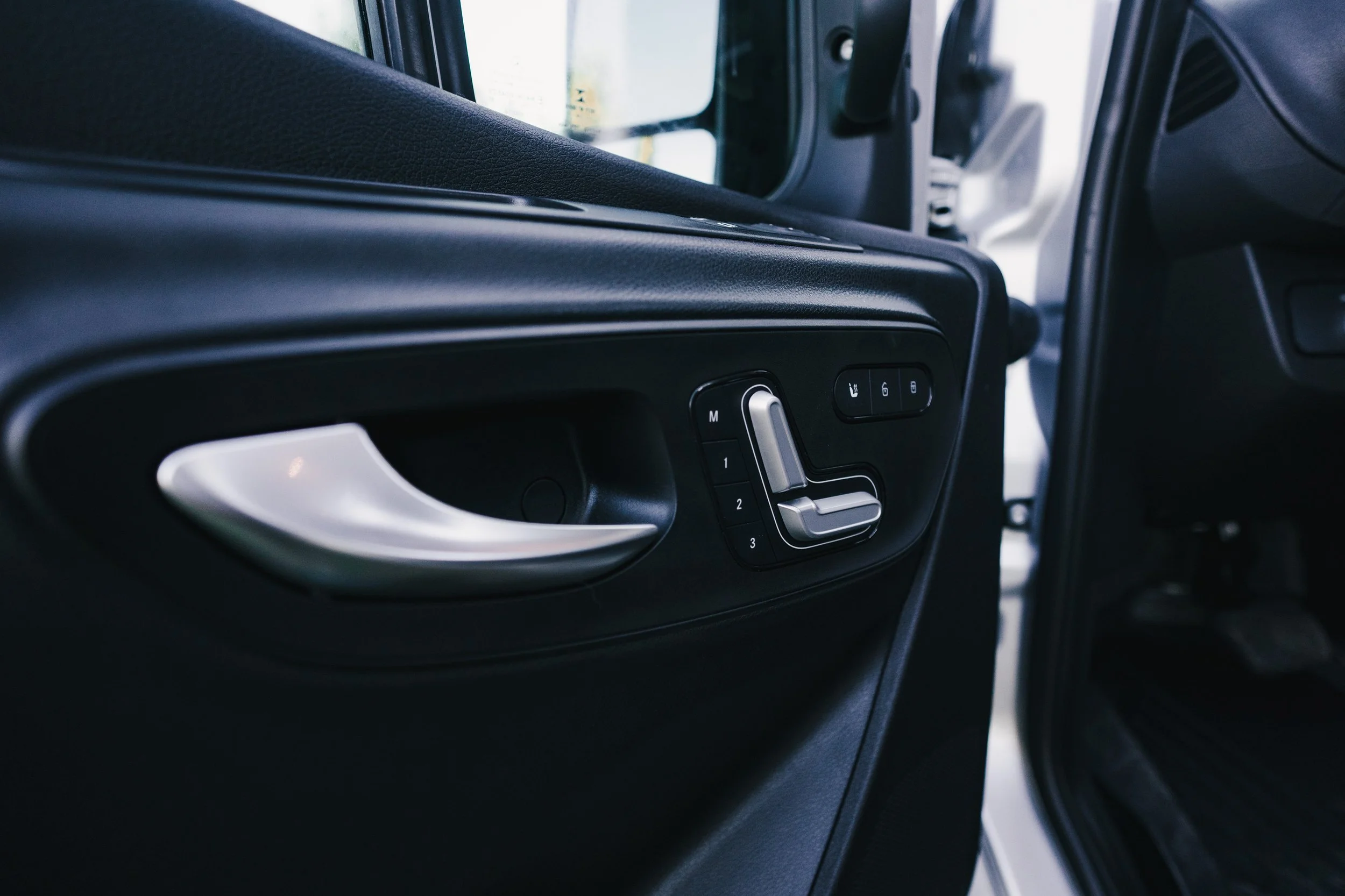 Interior of a vehicle door with seat memory buttons and window controls.