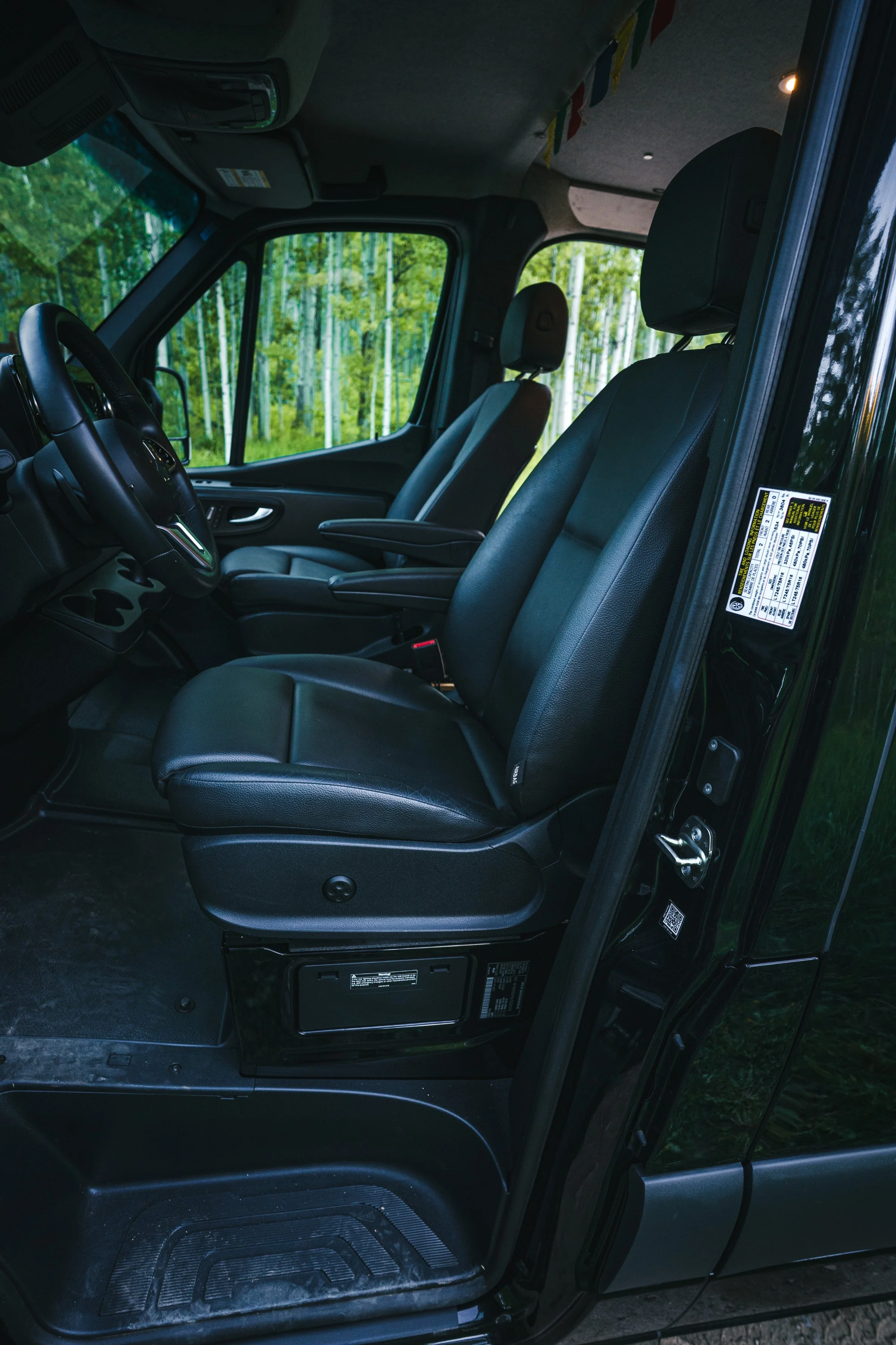 Interior of a vehicle showing black leather front seats, with a view of trees through the windows.