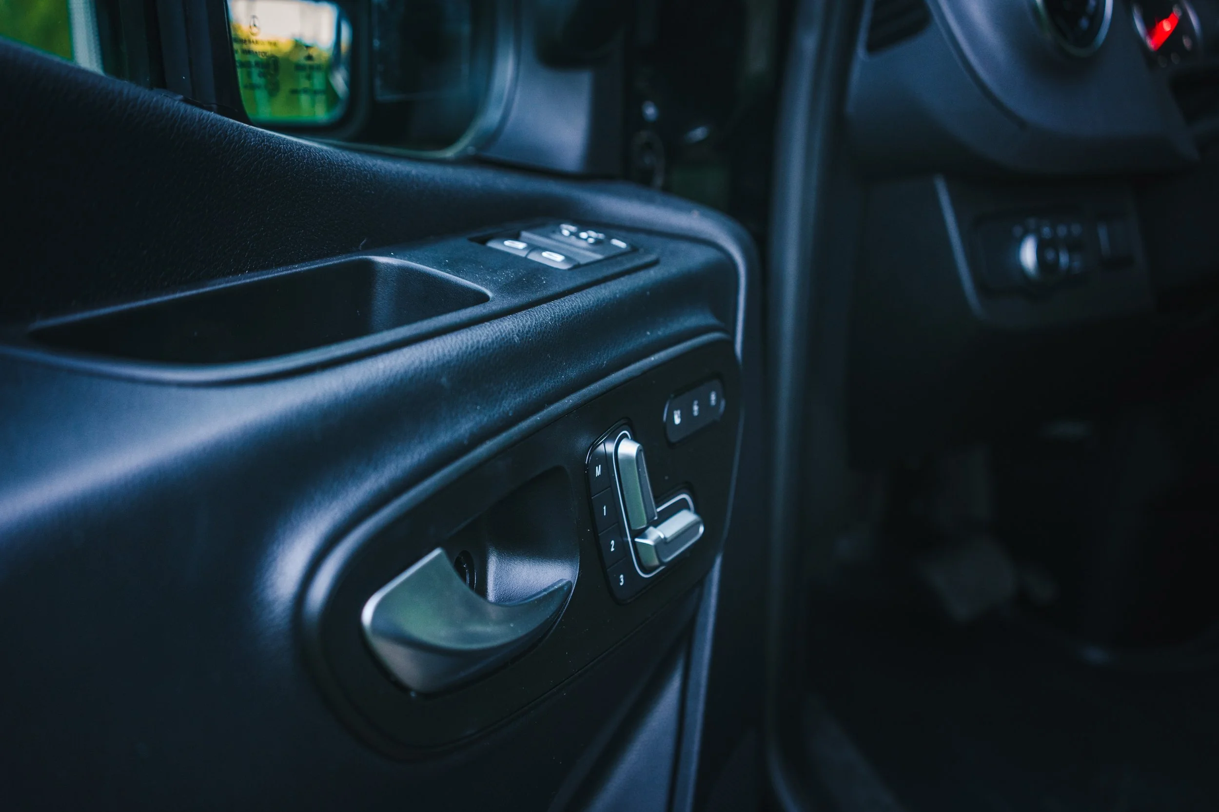 Interior of a vehicle showing a black dashboard with control panel, window switches, and a door handle.