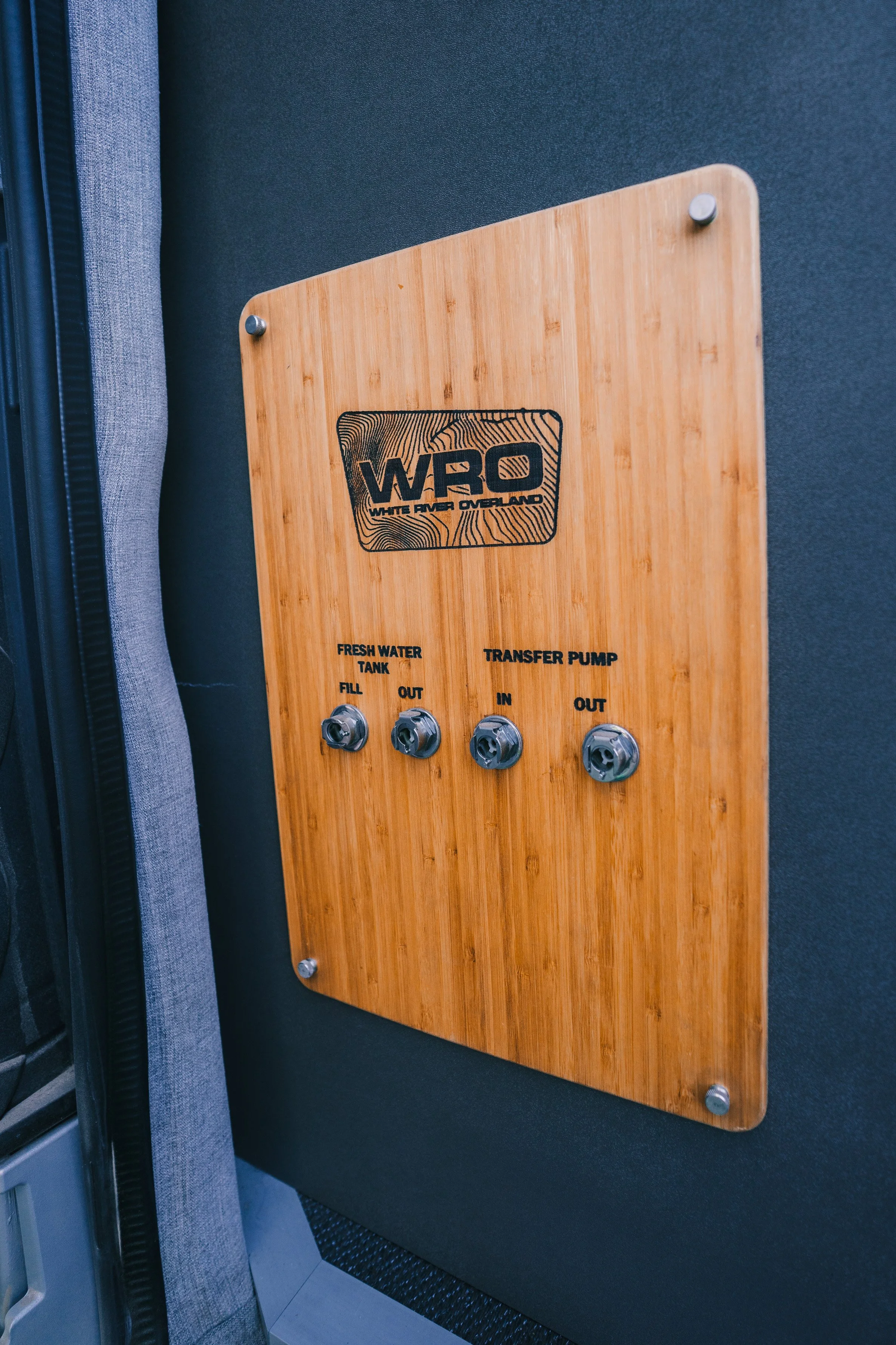 Wooden panel with switches and labels for a water system, including a fresh water tank fill and out, and a transfer pump in and out, with the logo 'WRO' for White River Overland.