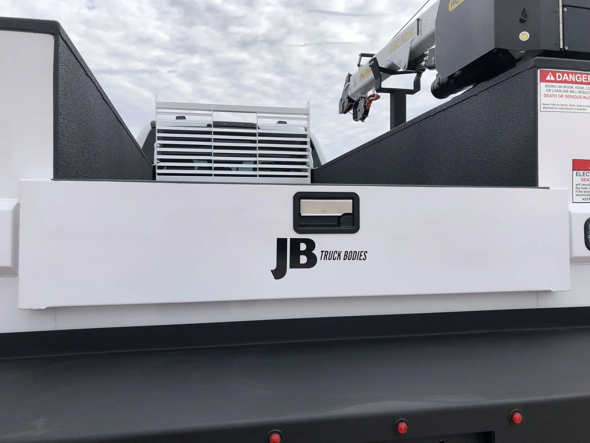 Close-up of the back of a utility truck or construction vehicle with the JB Truck Bodies logo and a trailer hitch.