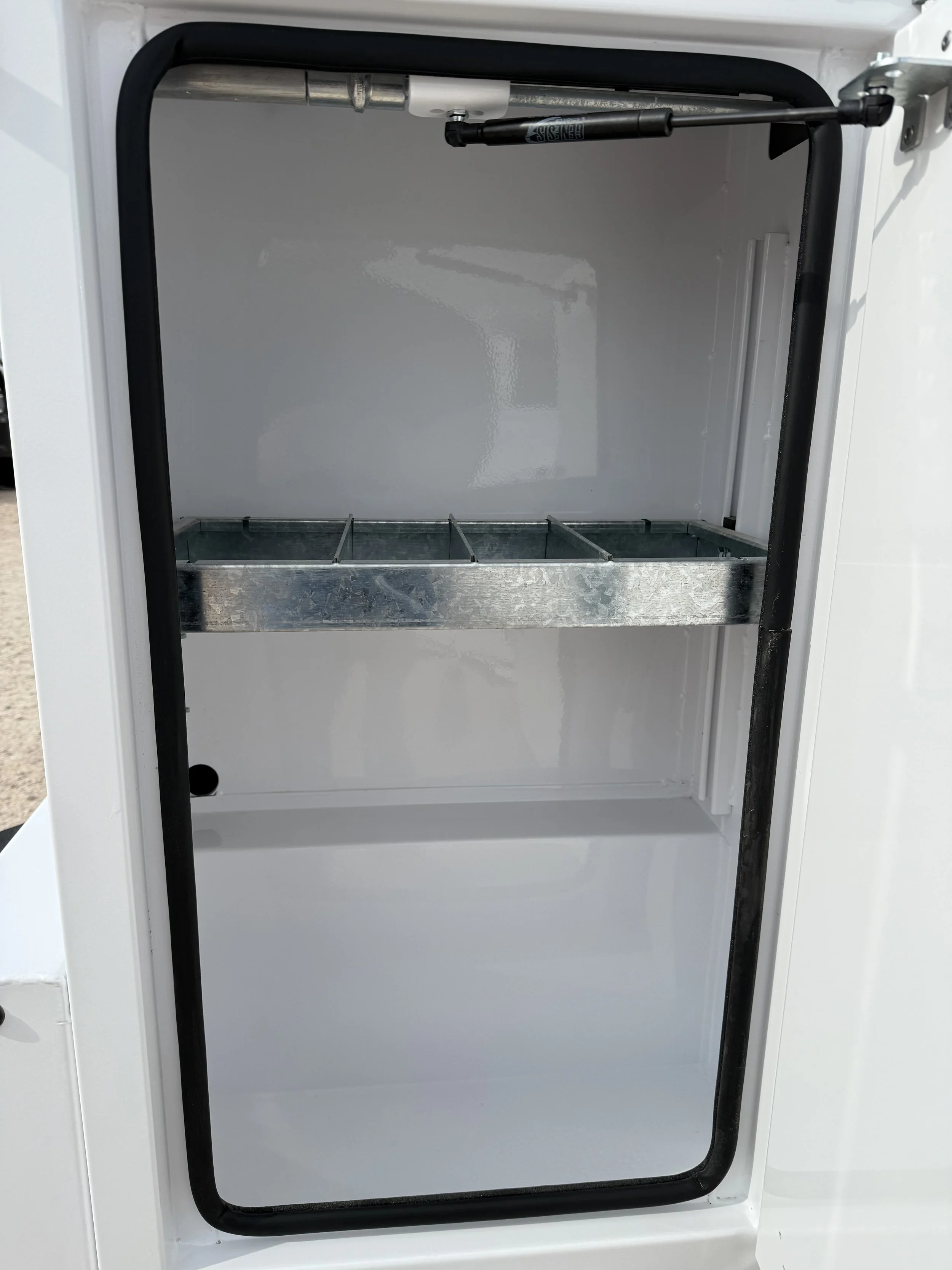 Empty white storage compartment with a black rubber seal and a metal shelf inside.