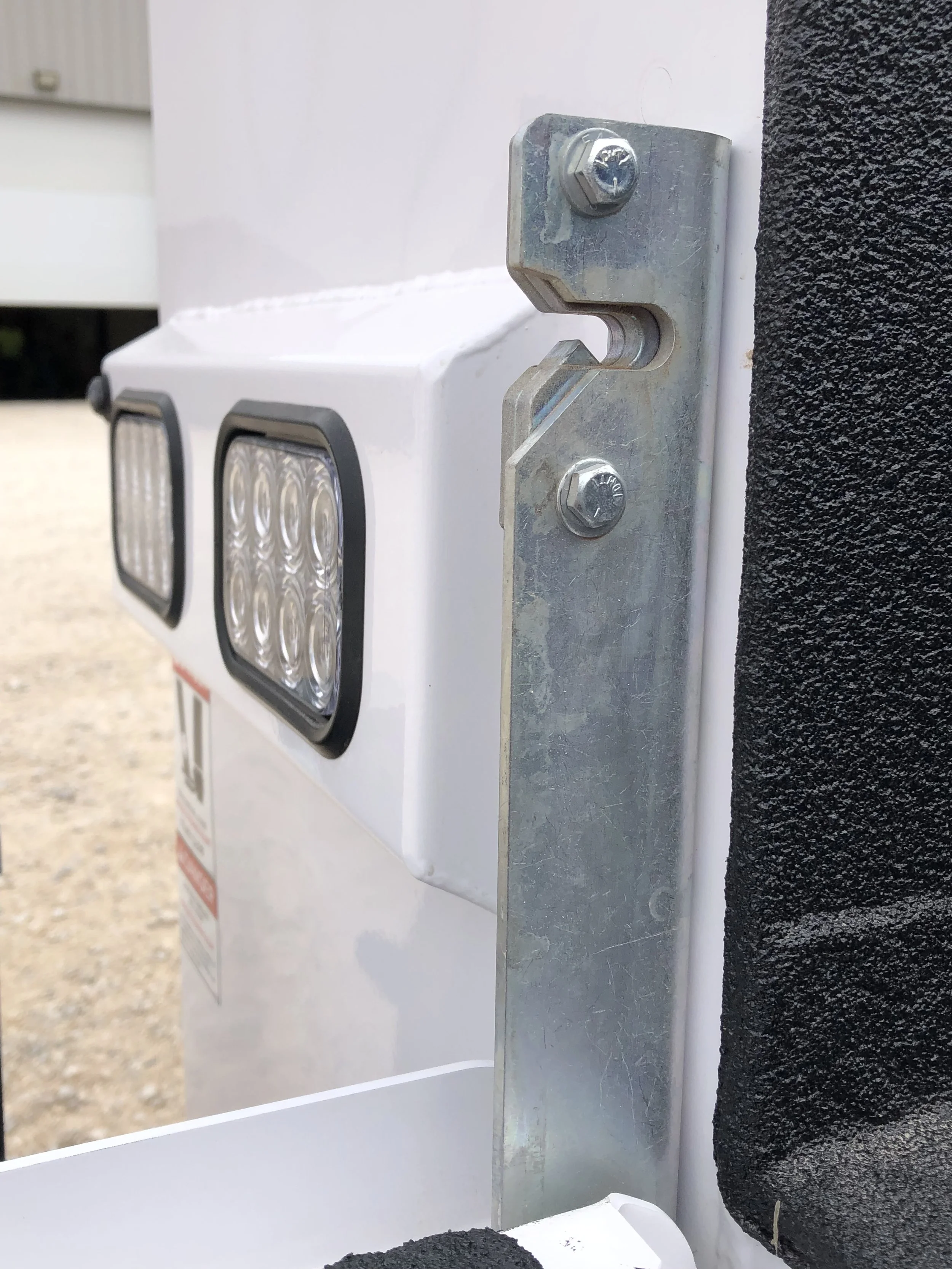 Close-up of a metal mounting bracket and electrical components on a white surface, possibly part of an outdoor electronic device or enclosure.