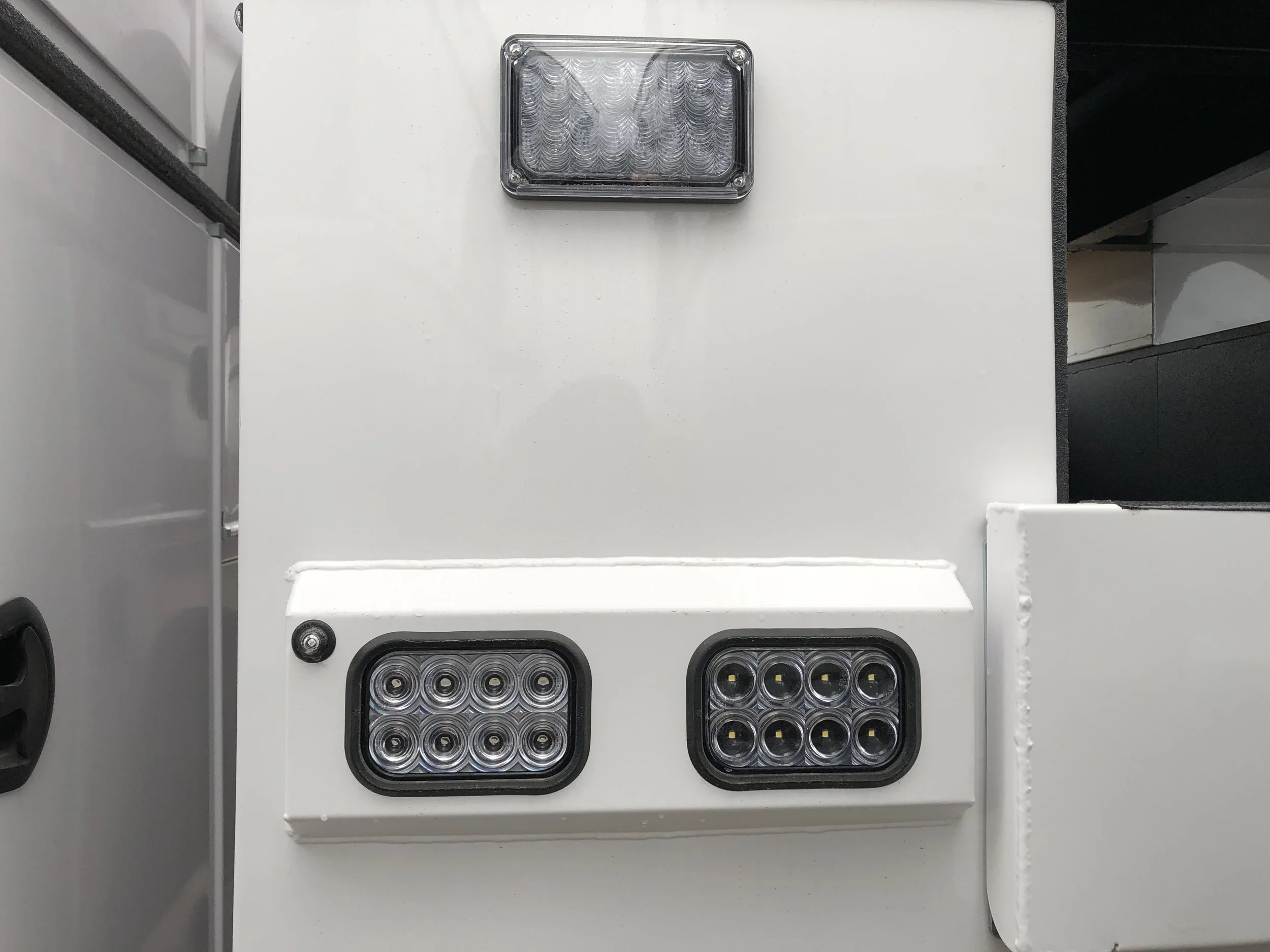 Close-up of a white electrical or industrial box with two sets of LED lights, one larger and one smaller, and a rectangular transparent cover on top.