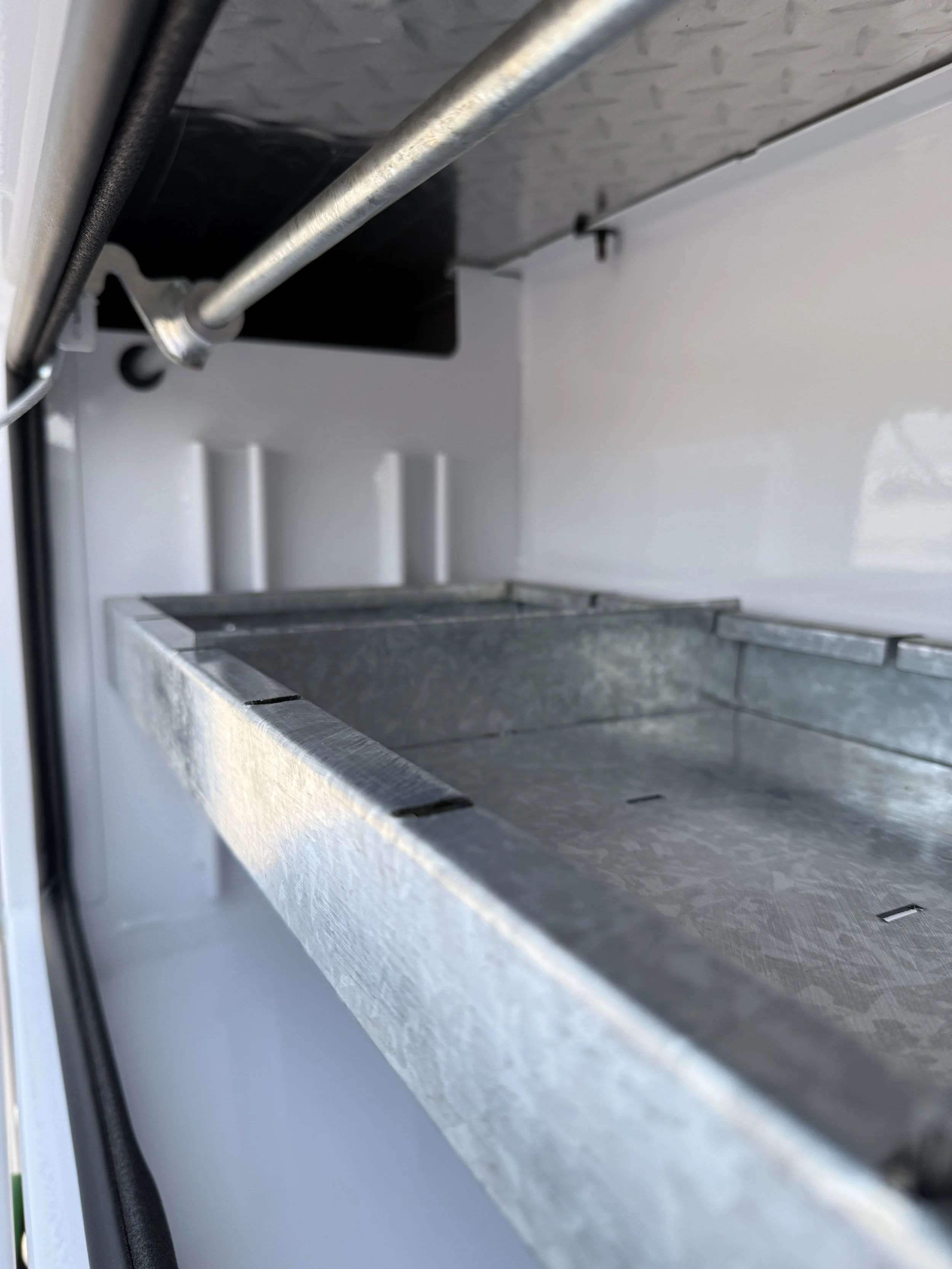 Close-up of an open ice maker with a metal ice tray, showing the interior and part of the drawer.