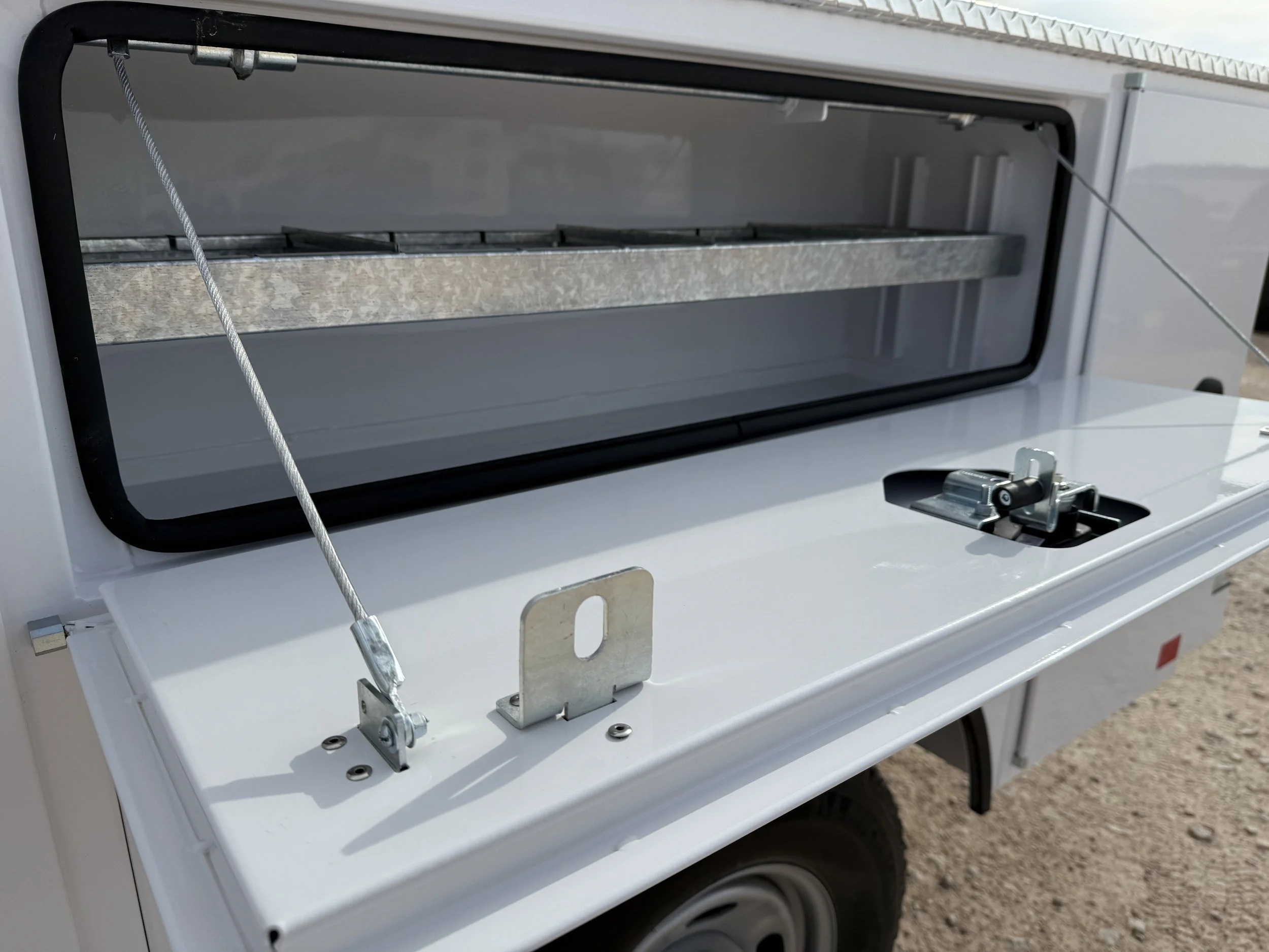 Open top of a white camper or trailer showing a storage compartment with a metal shelf and locking mechanisms.