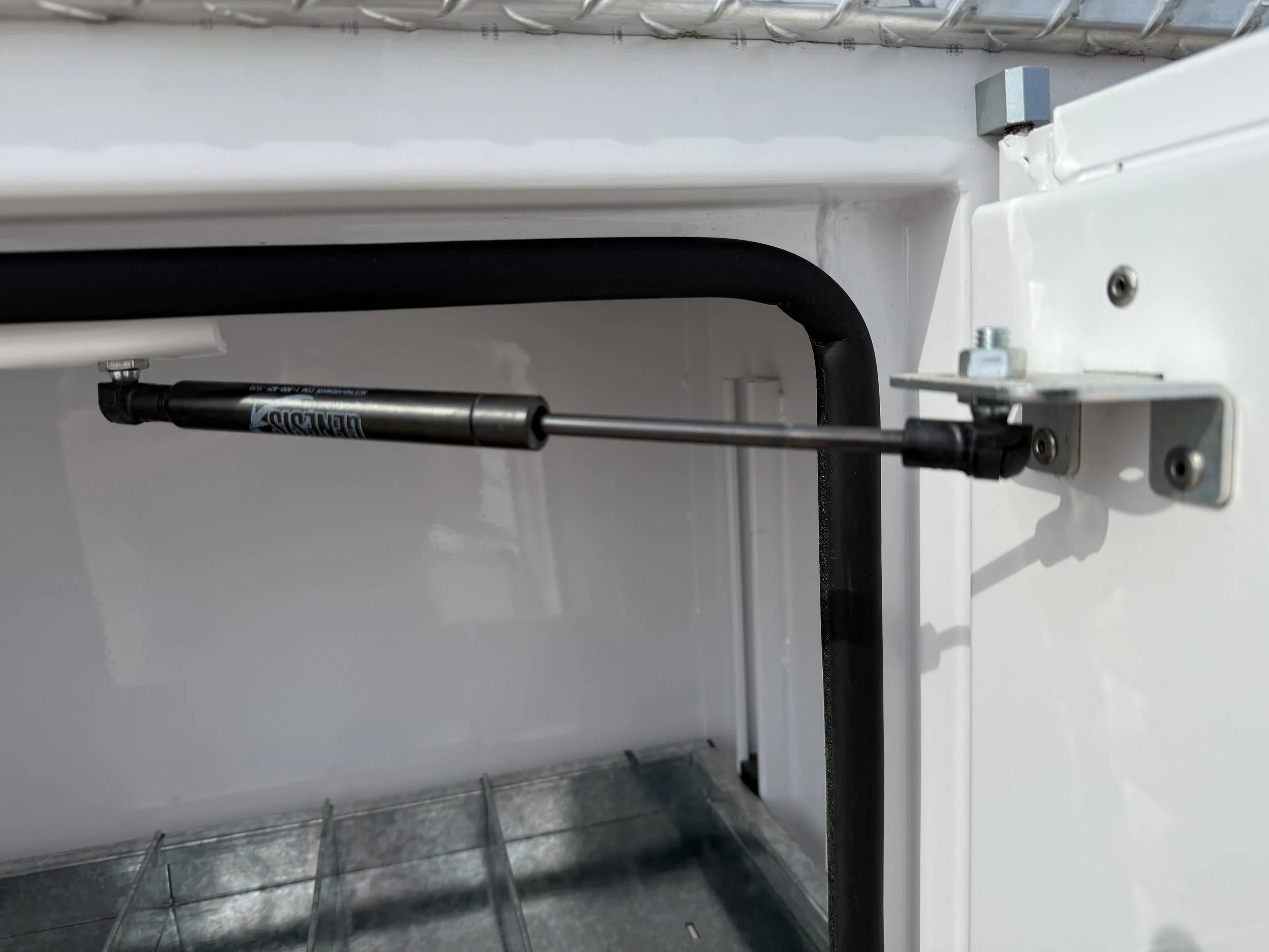 Close-up of an oven door with a gas strut attached to the metal hinge area for support.