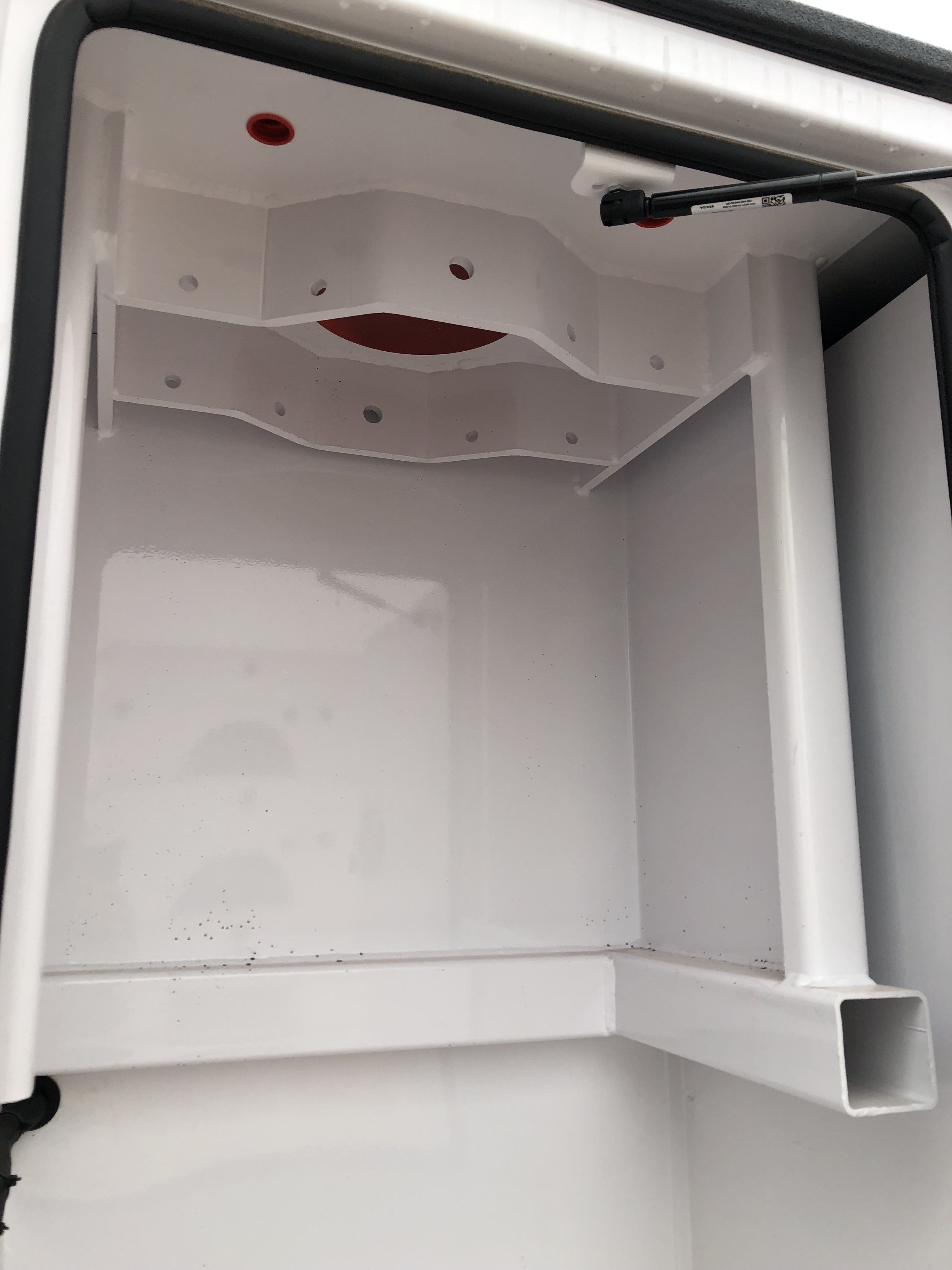 Empty white cabinet with a red circular opening at the top and a rectangular vent at the bottom right.