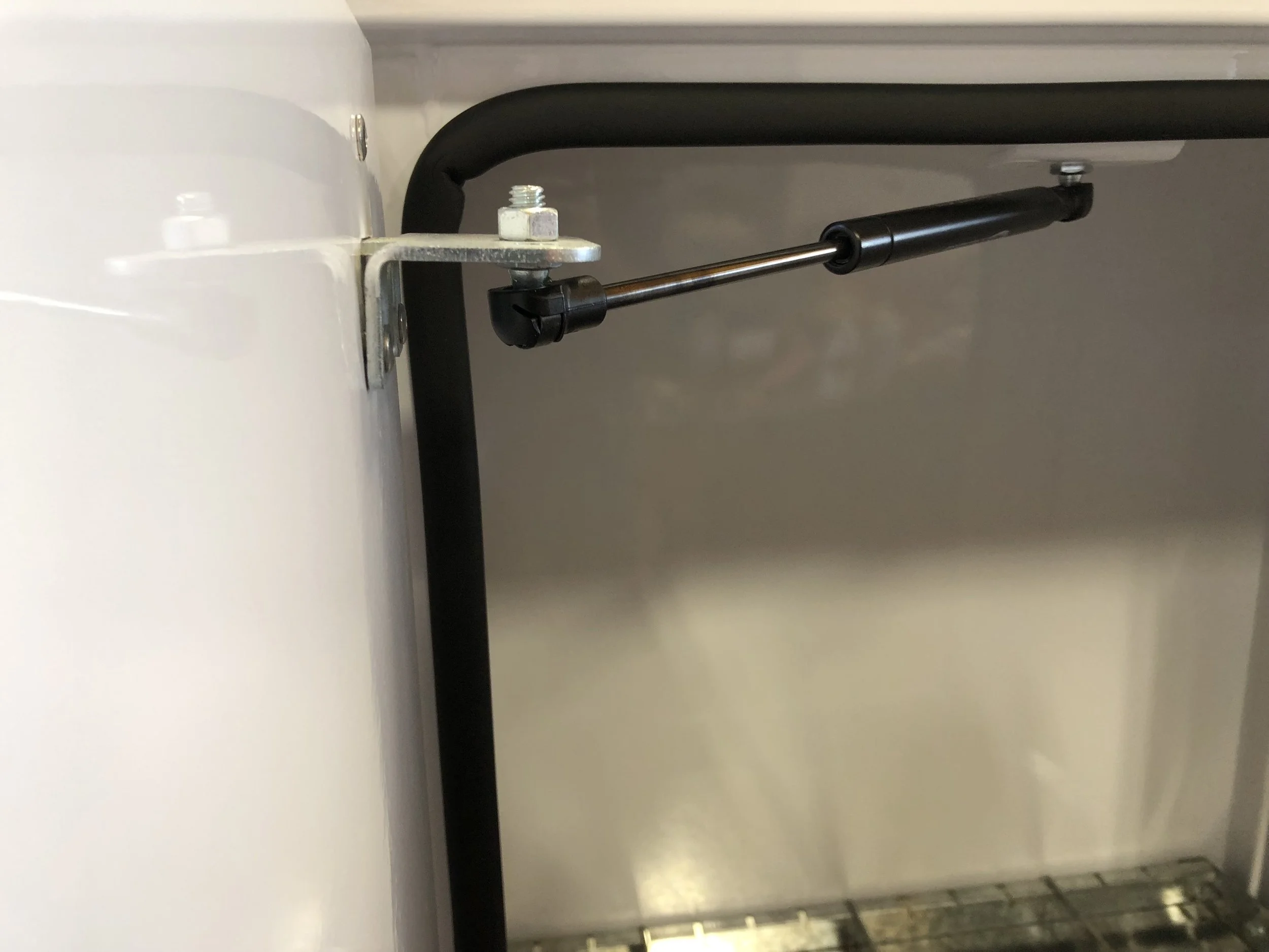 Close-up of a gas strut or hydraulic lift support attached to a white and black piece of equipment, possibly an industrial or medical device.