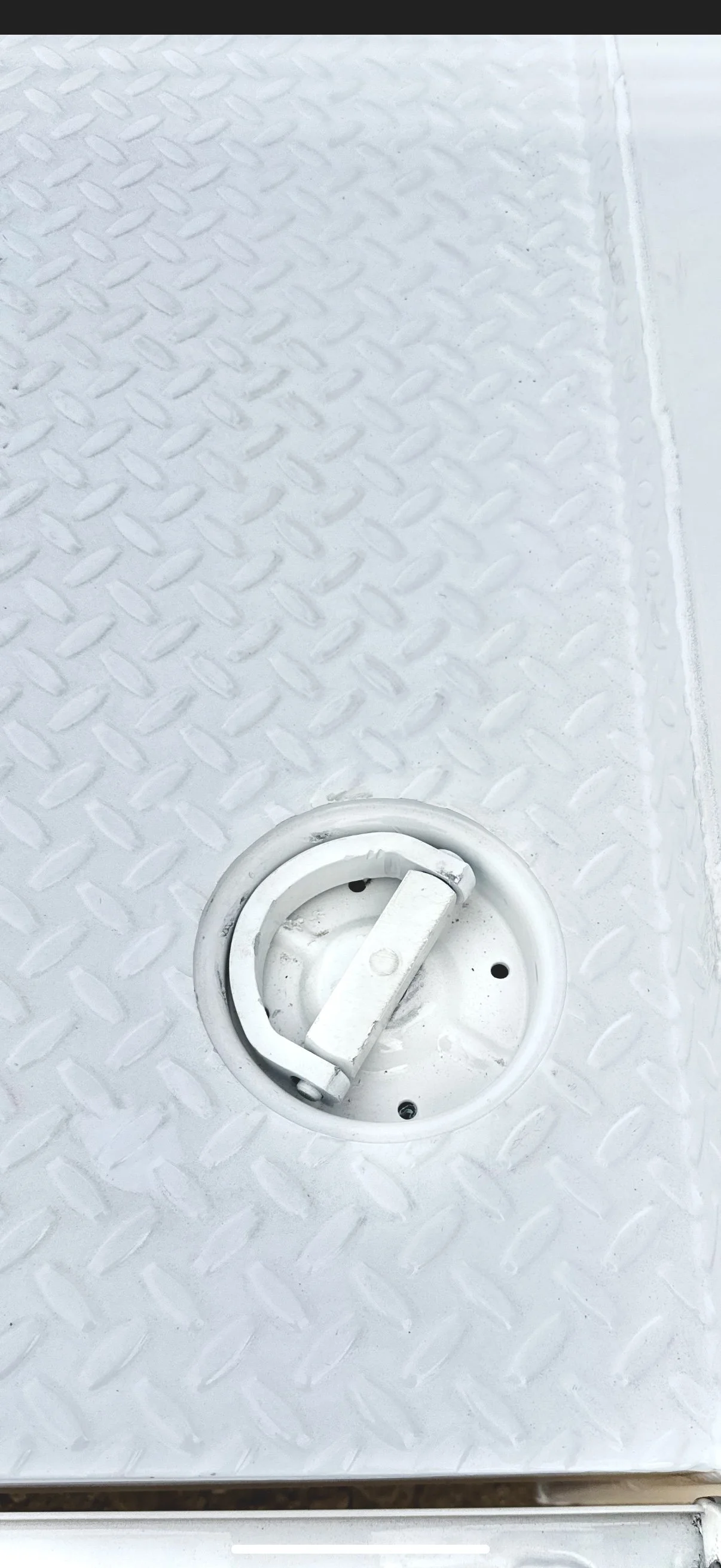 Close-up of a white, textured metal surface with a circular drain cover that has a latch handle.