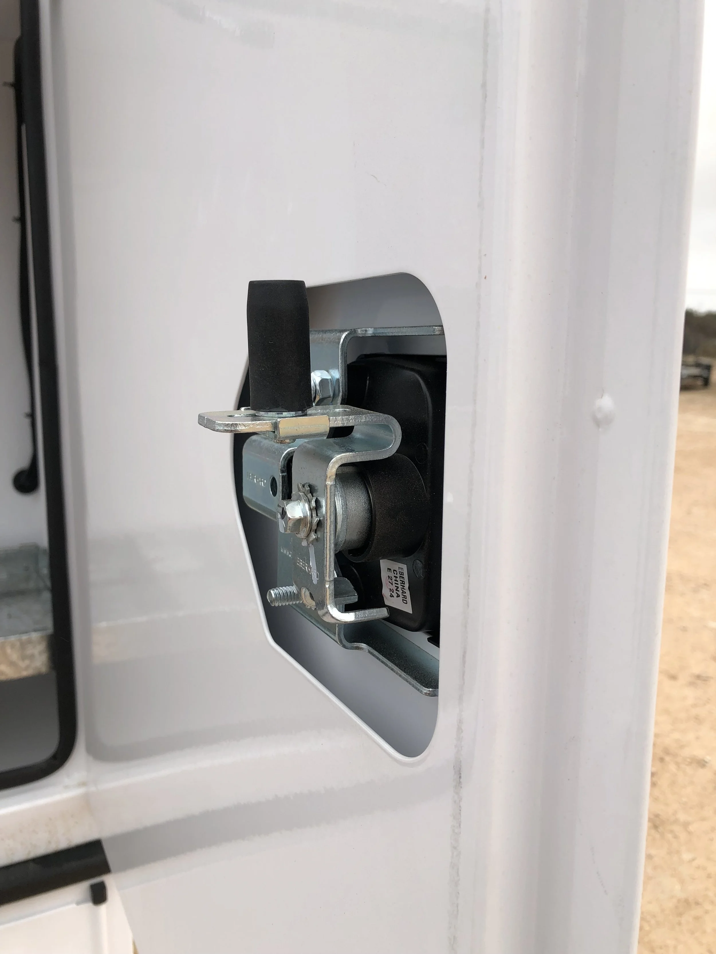 Close-up of a mechanical lock or latch system installed in a wall, with metal components and a black wheel or knob.