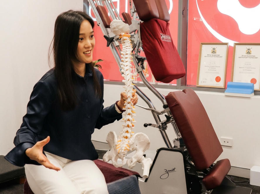 Experienced female chiropractor, Yu Jie, holds up a spine model to thoroughly explain a patient's condition, and provides recommendations for the patient.