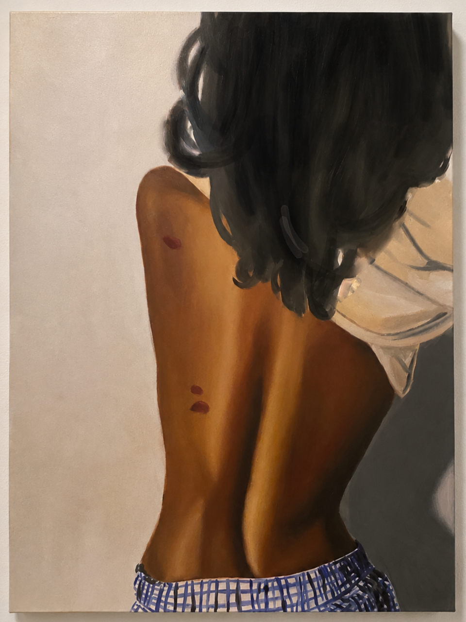 Painting of a woman with dark, curly hair and tan skin, viewed from behind, showing her back and shoulders, with a white top slipping off her shoulder and blue checkered shorts.