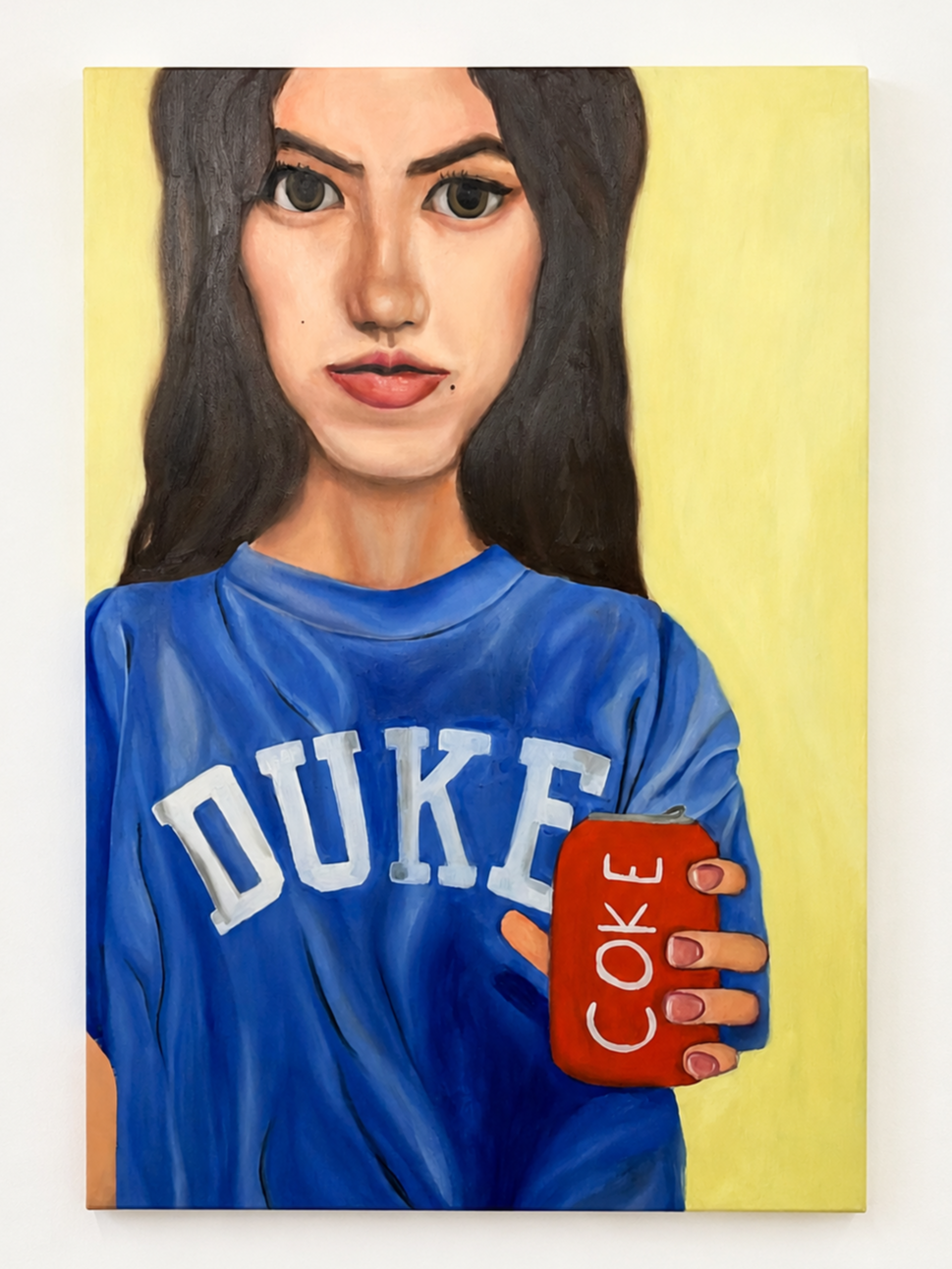 Portrait of a woman with long brown hair wearing a blue Duke University sweatshirt, holding a red phone with the word 'COOK' written on it, against a yellow background.