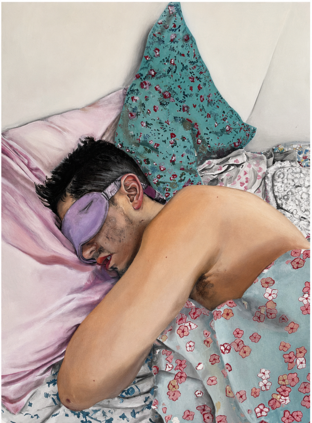 A man lying on his side on a bed, sleeping with a purple sleep mask covering his eyes. He is shirtless, with dark hair, and partially covered by a floral patterned blanket. There are pillows and a bedspread with floral designs in the background.