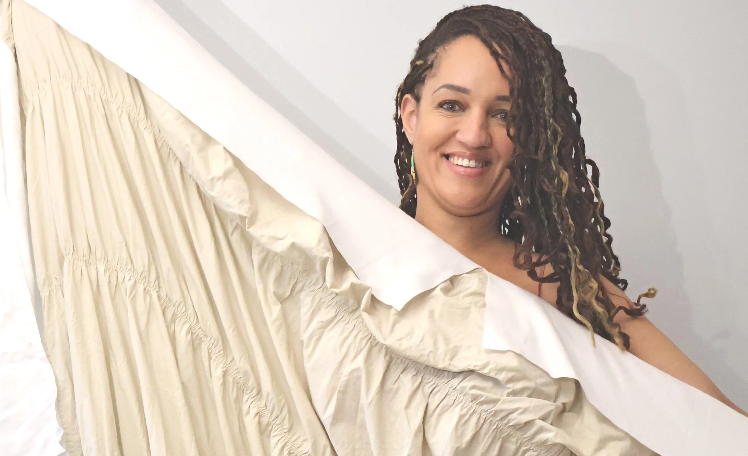 Woman with curly, dreadlocked hair smiling at camera, holding a thermonest