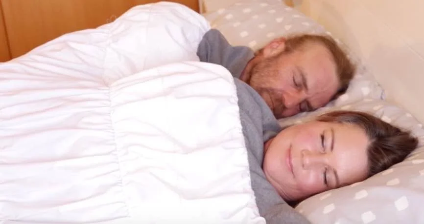 Two people sleeping in bed, covered with a thermonest, smiling peacefully.