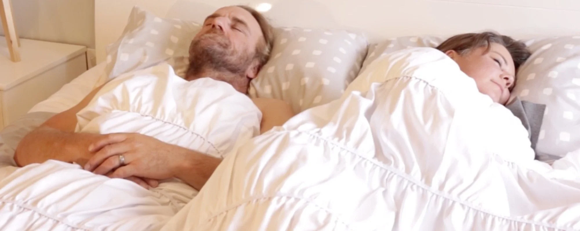 A middle-aged man and woman are sleeping together in bed with thermonest
