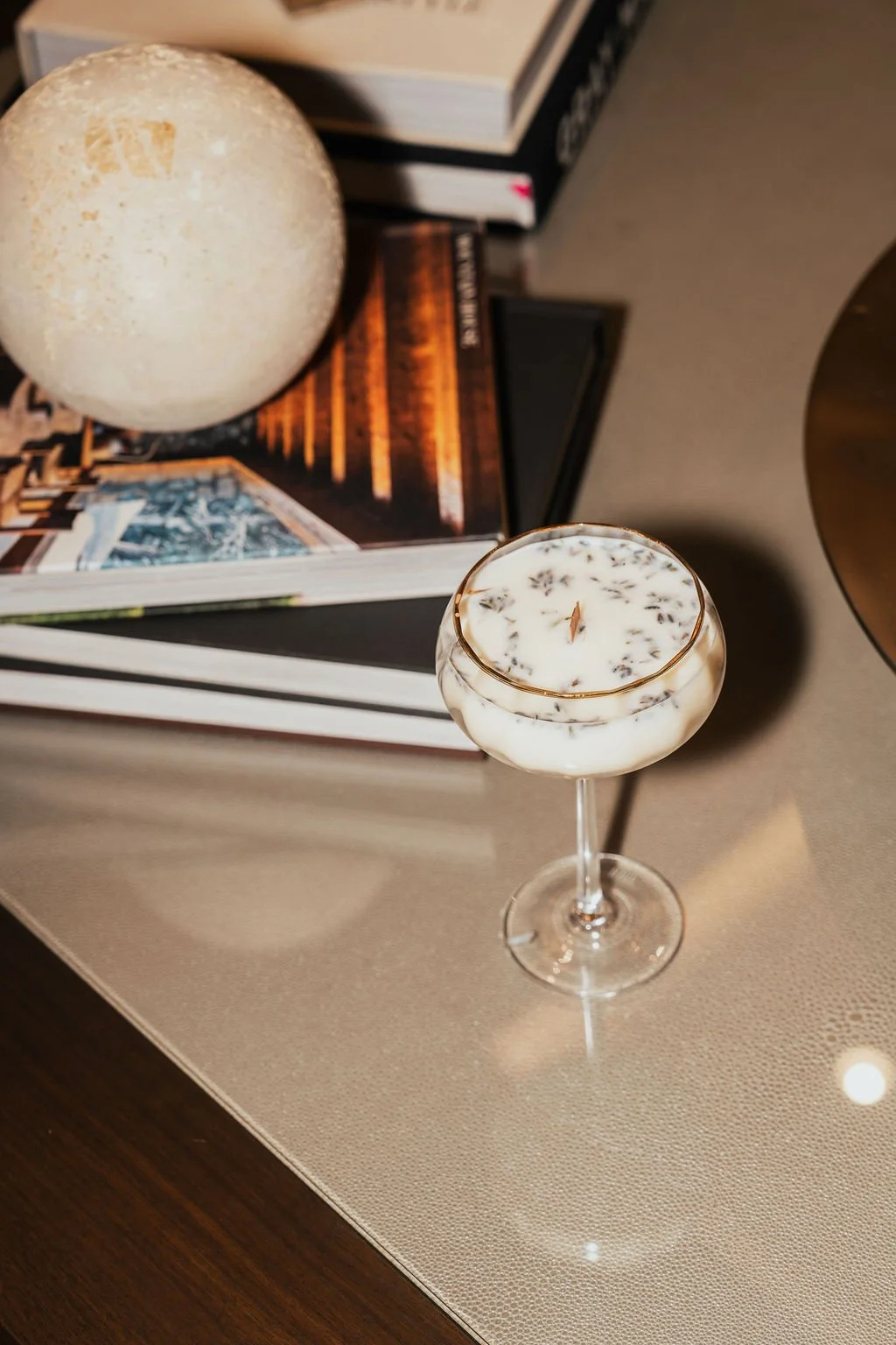 A Kandles2u candle in a glass holder, books, and a decorative sphere on a table.