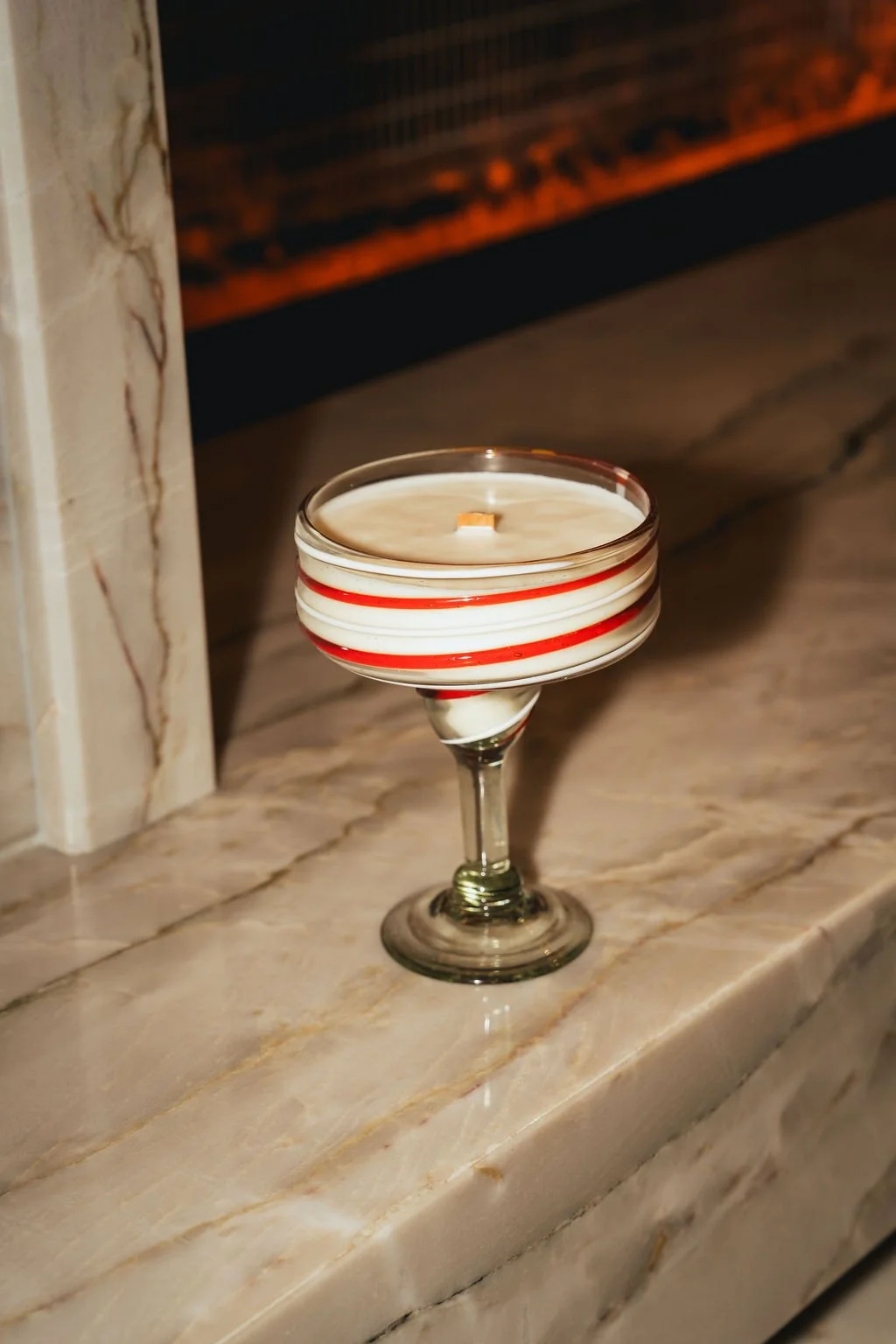 A candle in a glass holder with red and white stripes, placed on a marble surface.