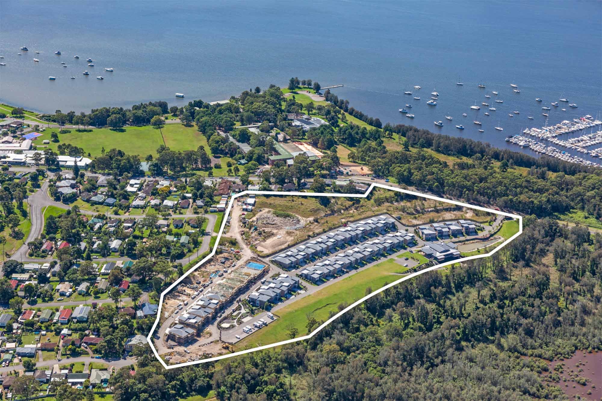 Aerial view of a residential area near a body of water, with a section outlining a new housing development under construction.
