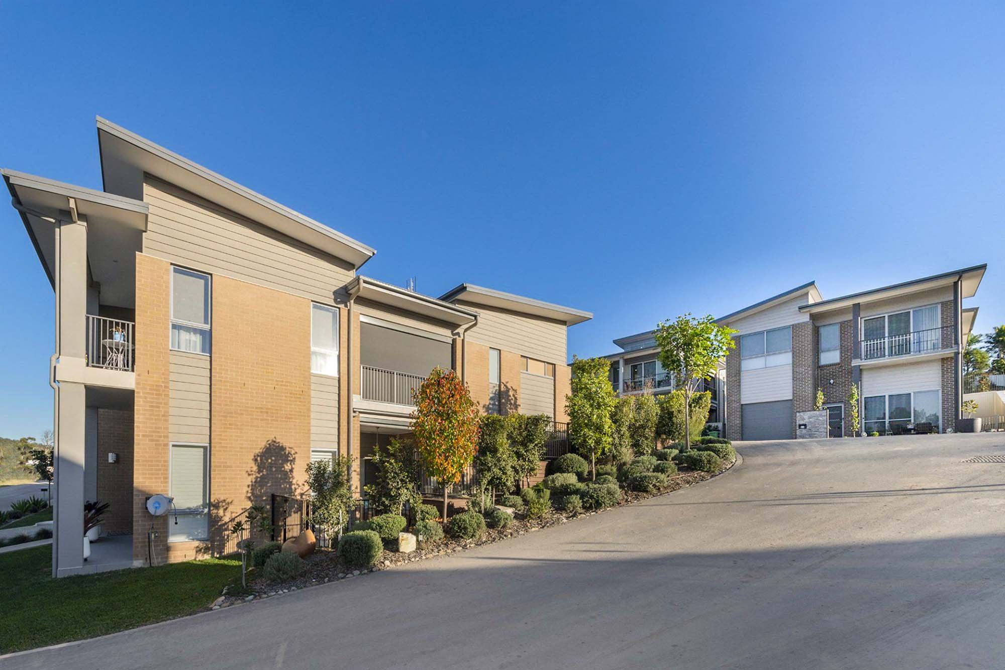 Modern multi-family residential buildings with landscaped yard, on a bright sunny day under a clear blue sky.