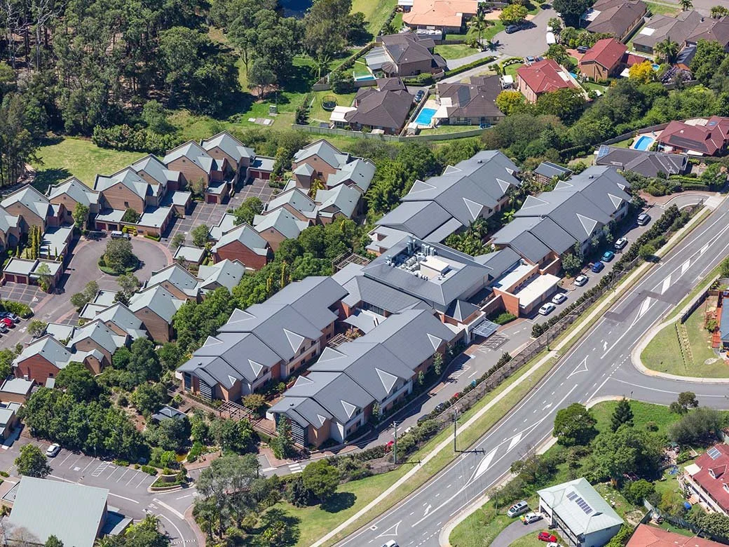 Aerial view of a residential neighborhood with houses, greenery, and a main road.