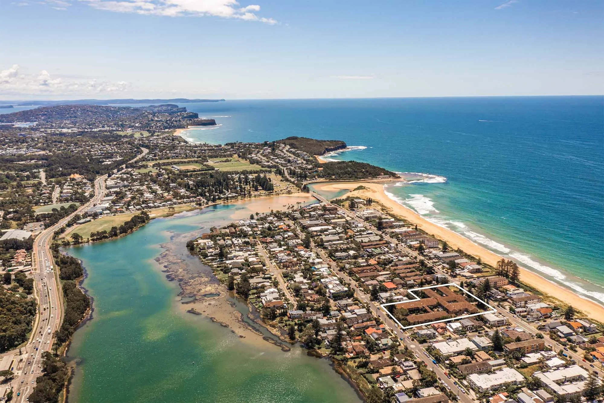 Aerial view of a coastal city with river, beach, and ocean, showing residential streets and buildings near the shoreline.