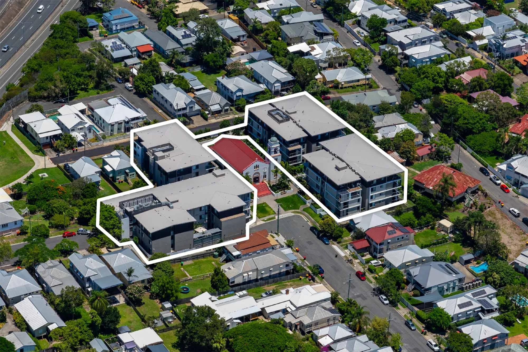 Aerial view of a residential neighborhood with a large complex outlined in white, featuring multiple buildings, green spaces, and trees.