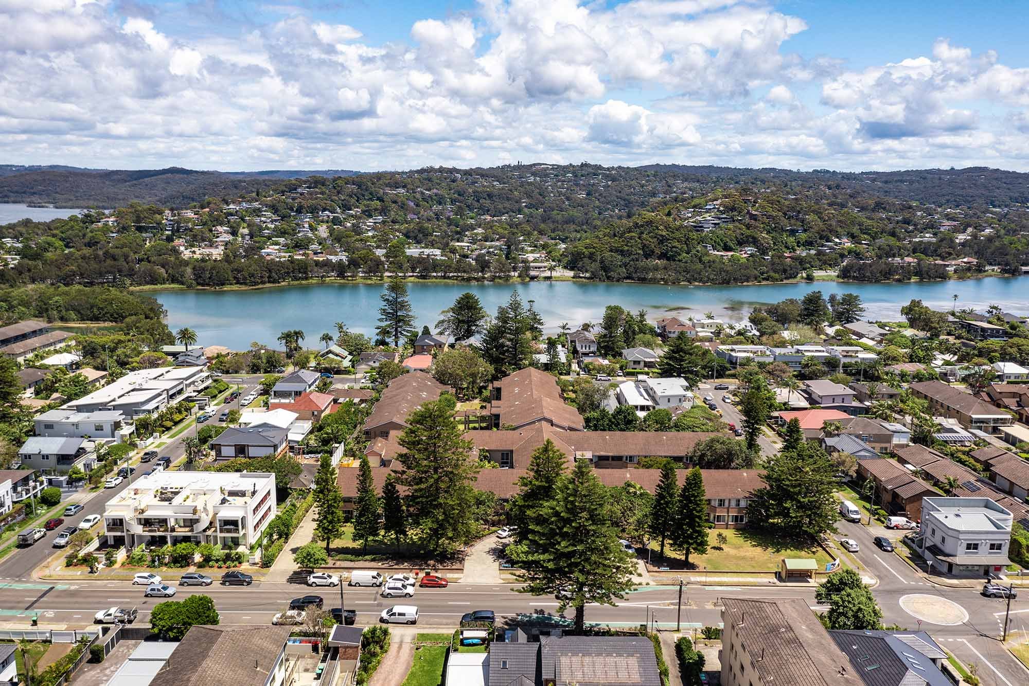 Aerial view of a suburban neighborhood with a lake in the background, surrounded by hills and partly cloudy sky.
